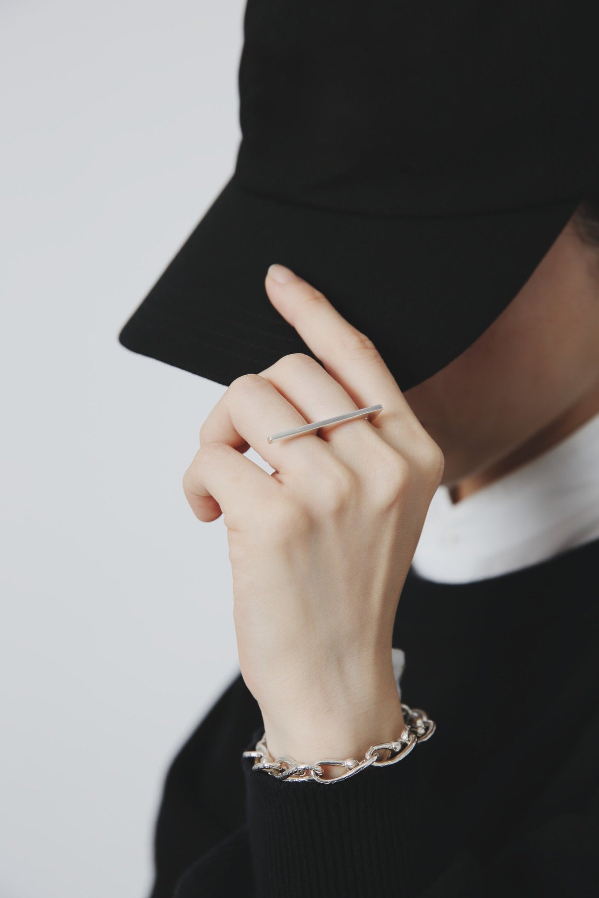 Nine Nineのシルバー925リング(ダブルリング)を着用して黒い帽子のつばに手を添えた写真。手首にはチェーンブレスレット。