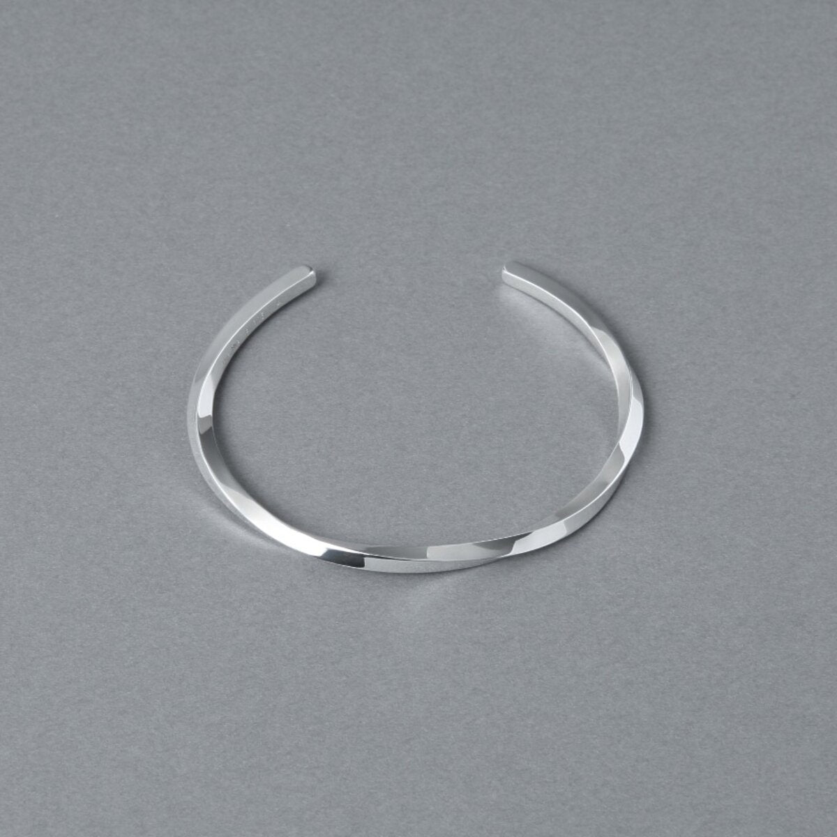 シルバー925バングル「21-B-005」(幅3mm)を、開口部を上に向けてグレー背景で上方から撮影。ねじりのあるフォルムと鏡面仕上げの輝き、全体の形状が見える商品写真。