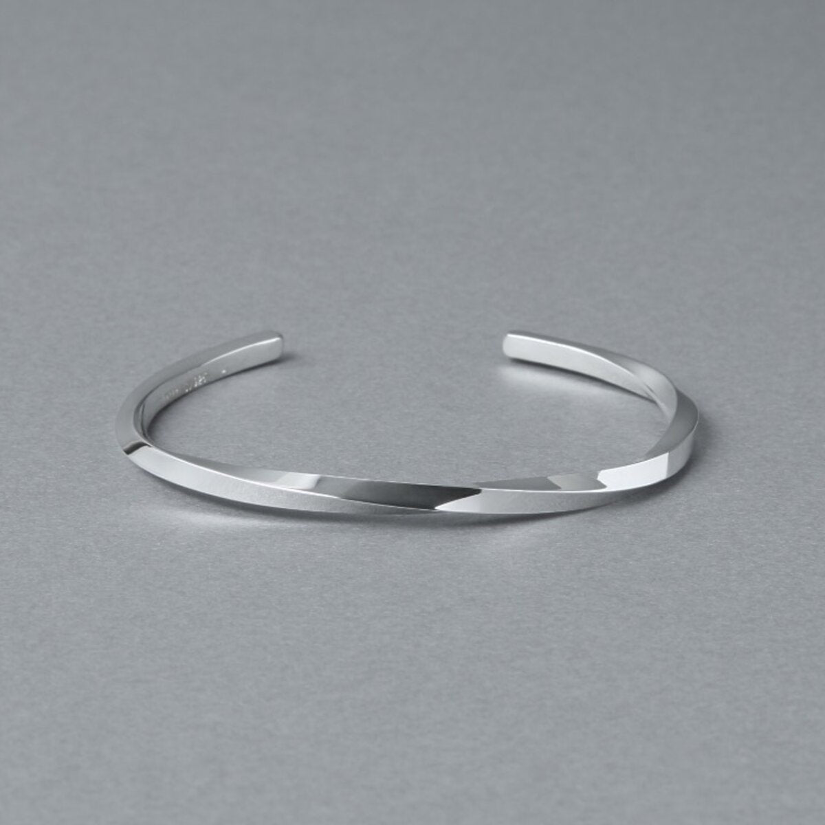 シルバー925バングル「21-B-005」(幅3mm)の商品写真。ねじりのあるフォルムと鏡面仕上げの輝き、開口部をグレー背景で斜め上から撮影。