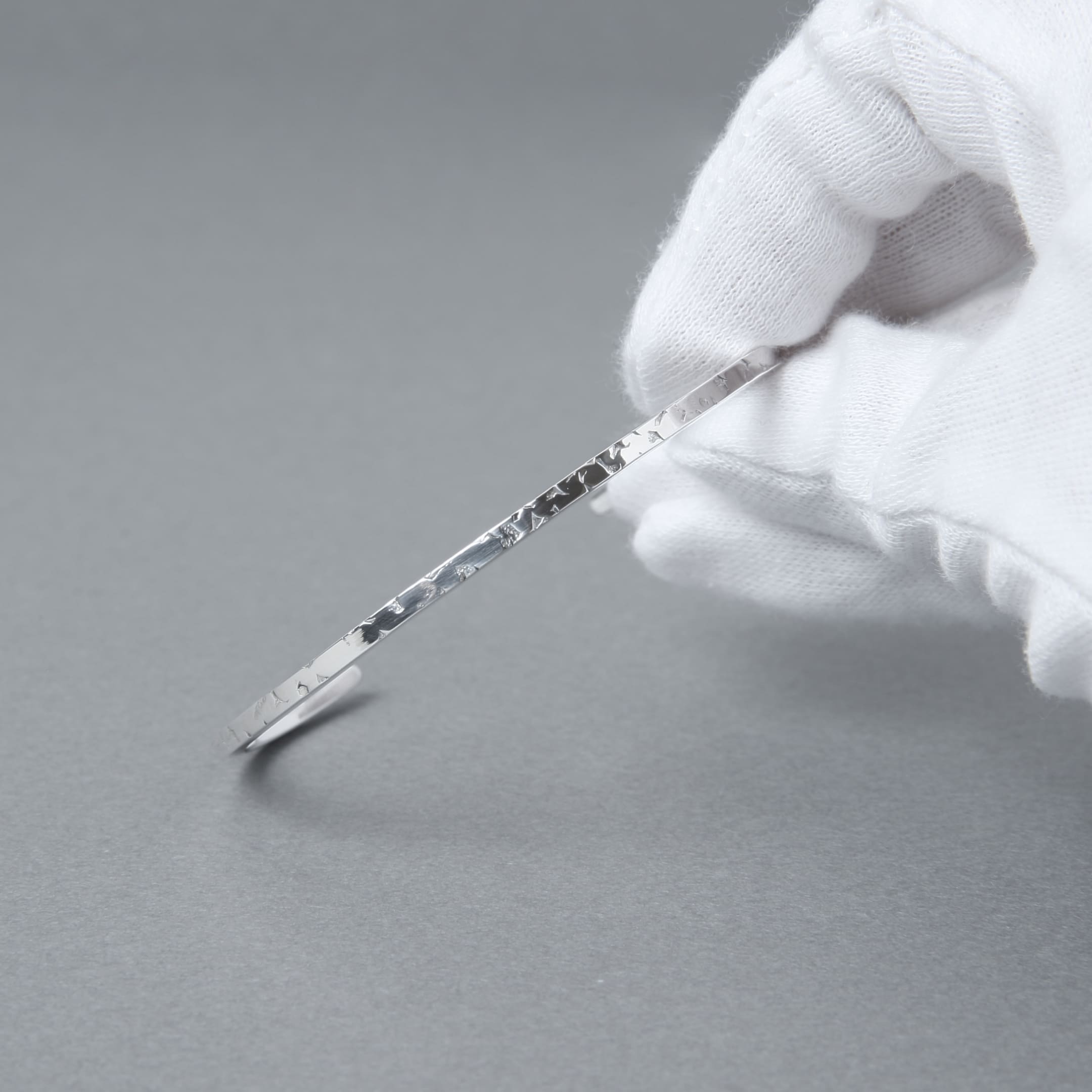 手袋を着用した手で持ったシルバー925細身バングルの質感クローズアップ写真