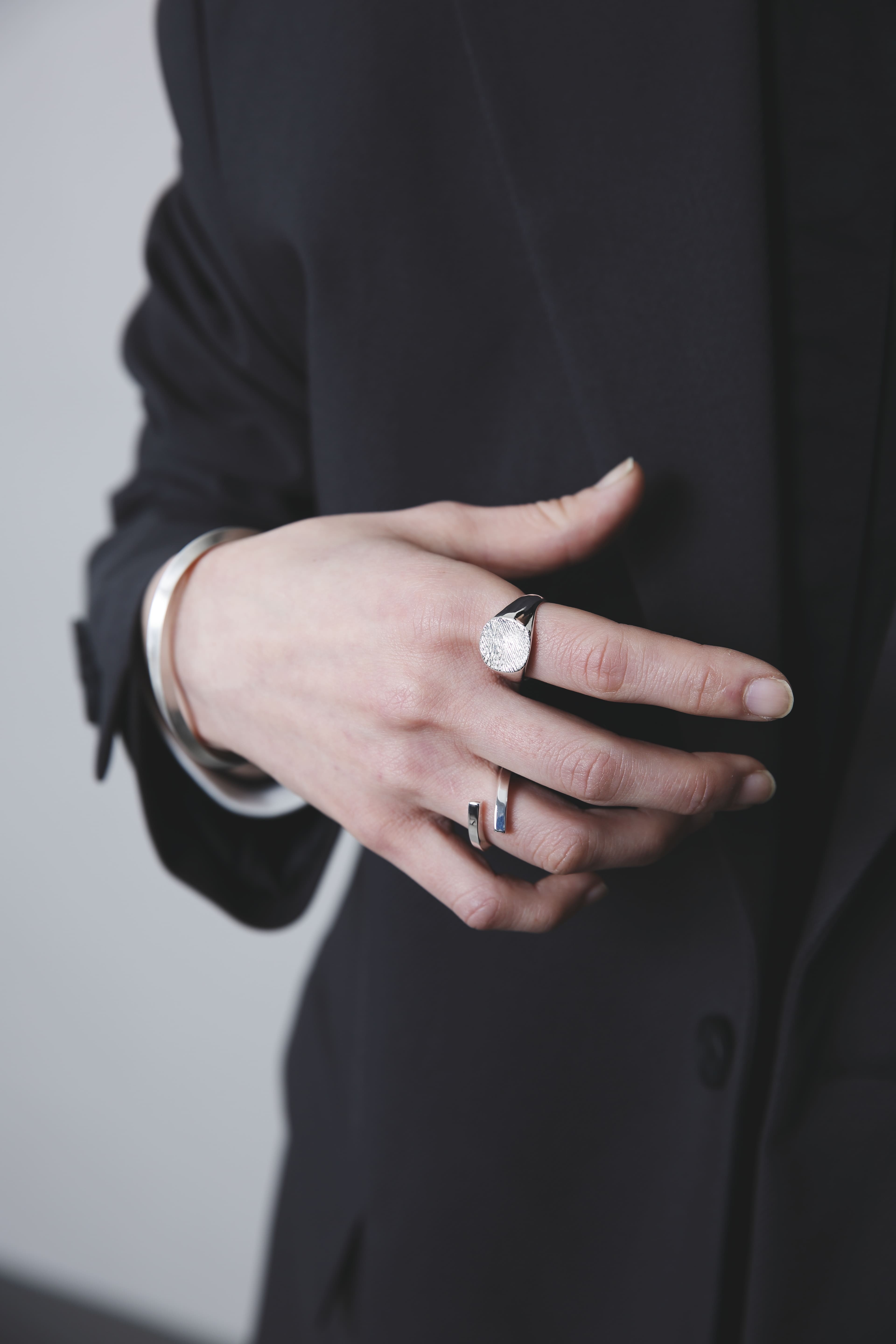 丸い木目模様のシグネットリングとオープンリング、そしてシルバーバングルを合わせたコーディネートが、落ち着いたトーンの中に個性を添える。