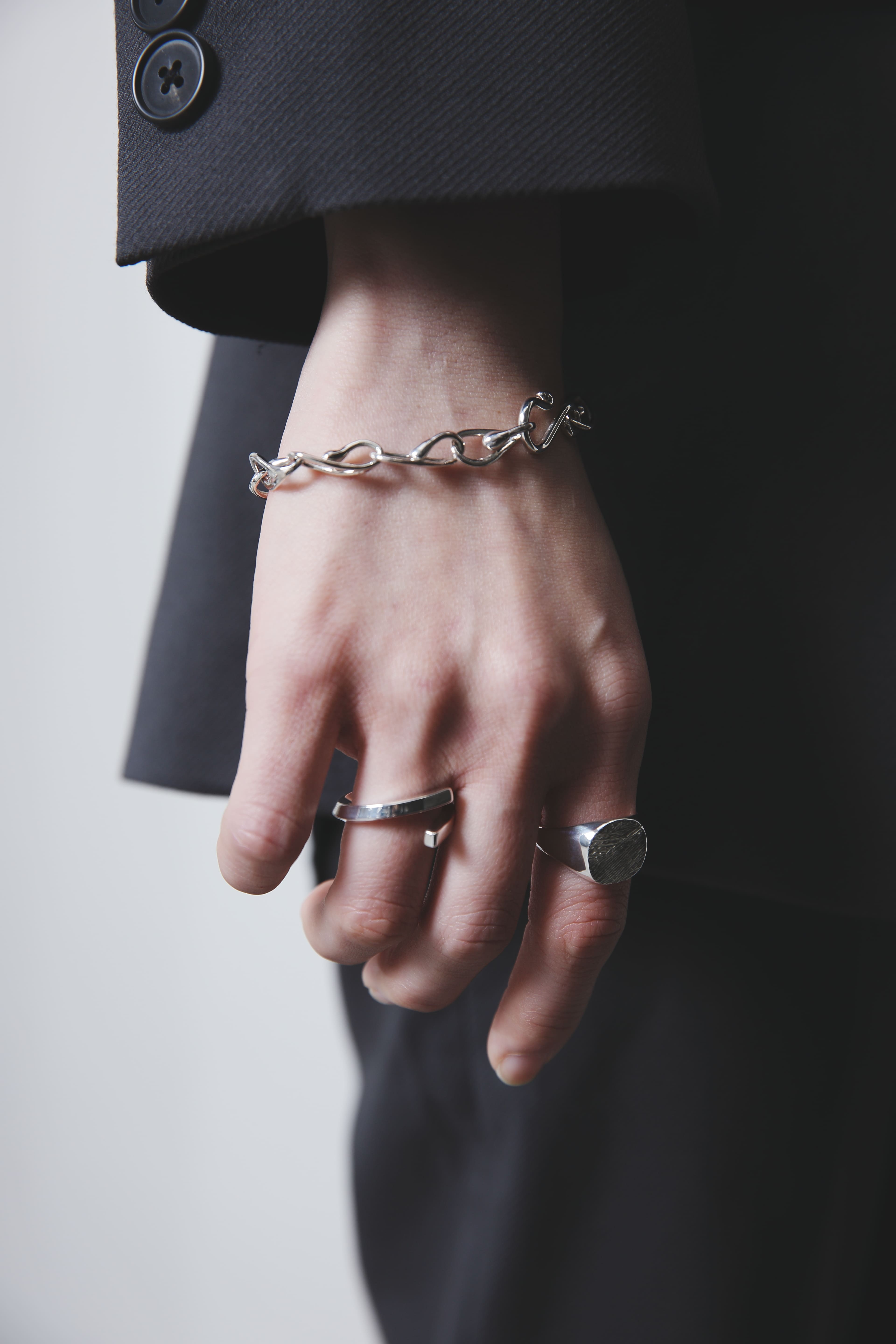 チェーンリンクデザインのシルバーブレスレットと、質感の異なる2つのシルバーリングを重ね付けした手元。丸いトップの木目模様リングが印象的で、ミニマルながら個性を感じるスタイル。