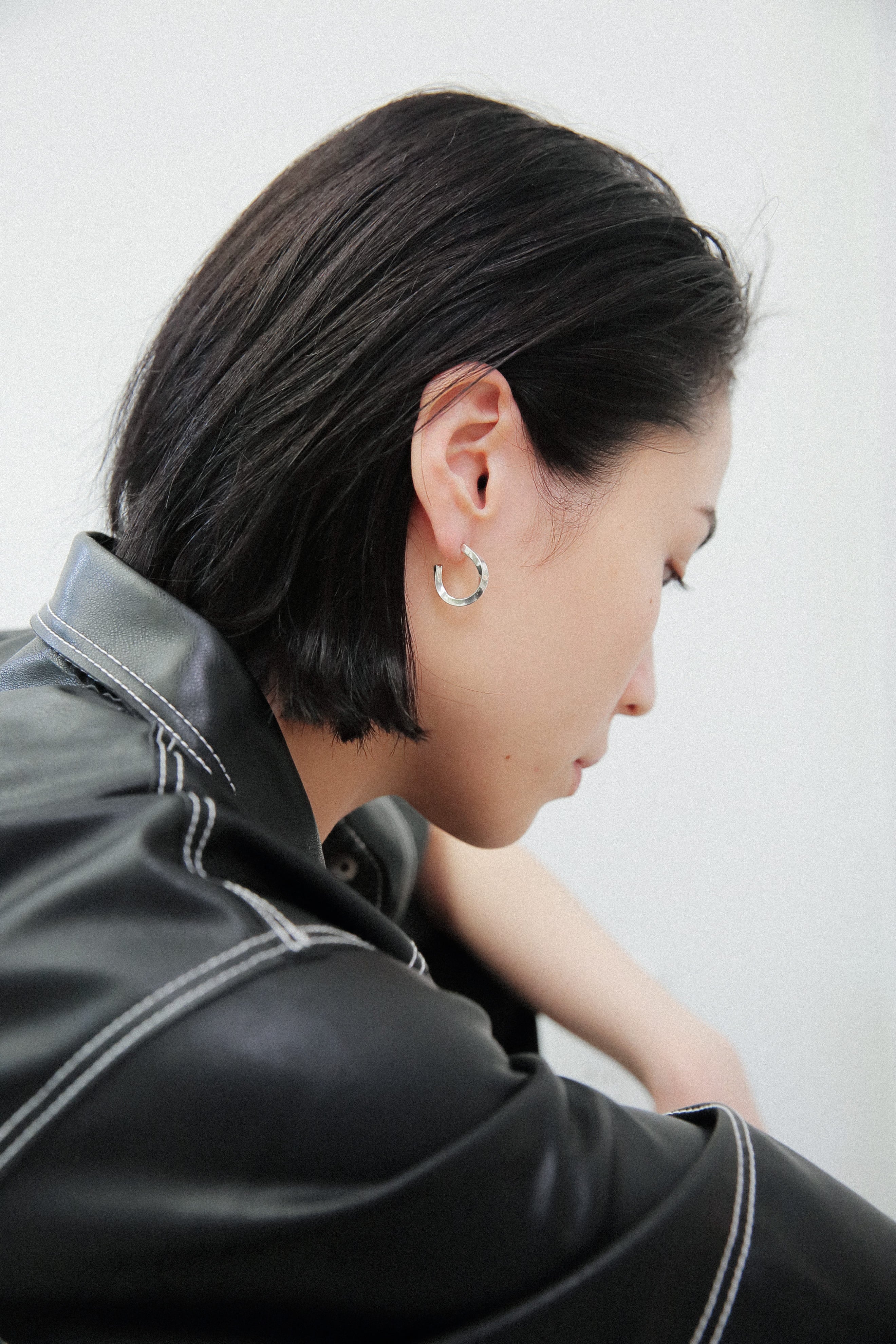黒のレザージャケットを羽織った女性の横顔。耳元には、重厚感のあるシルバー925のフープピアスが輝き、洗練された都会的な印象を与えている。