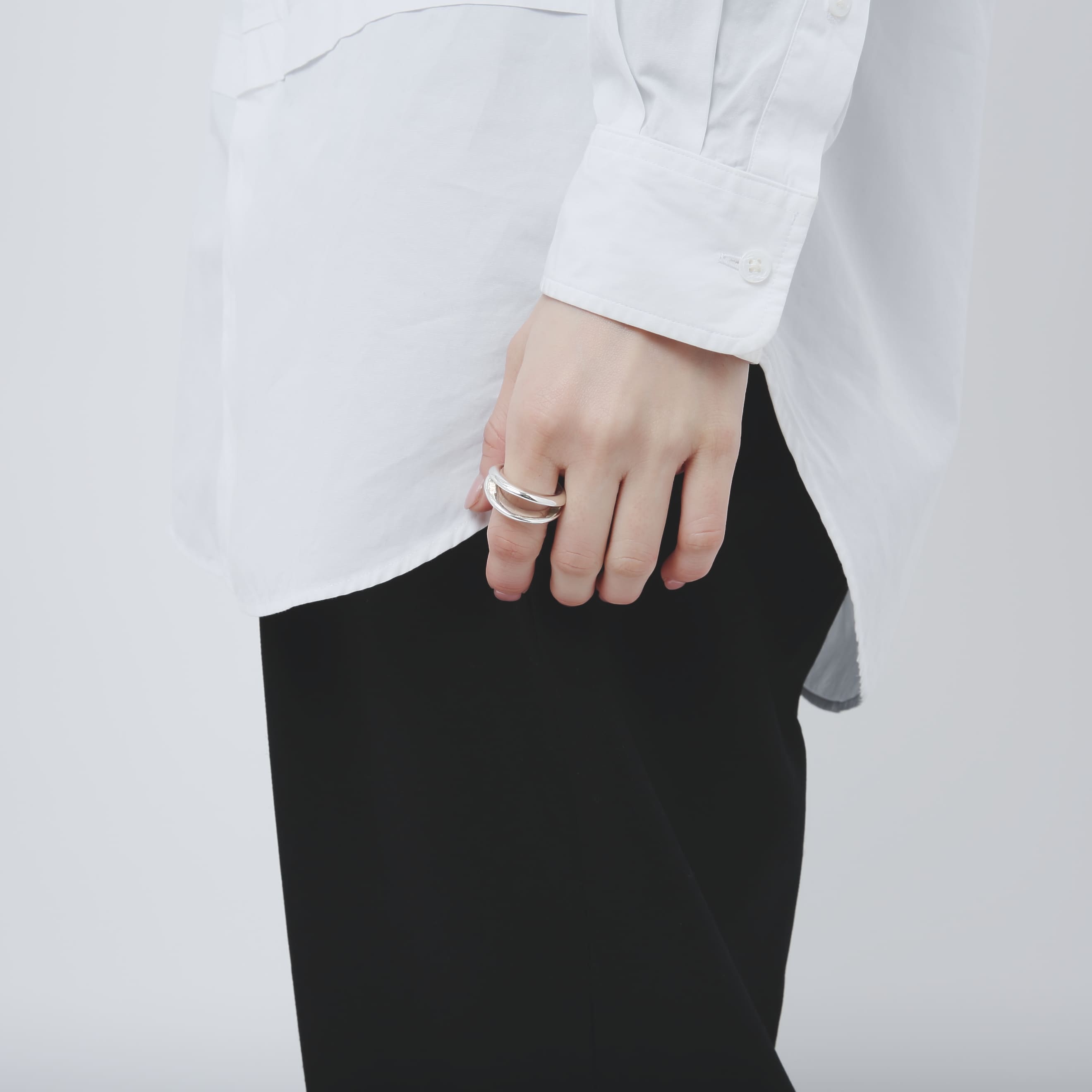 モデルの全身に近い立ち姿での手元カット。白シャツと黒のボトムスに、シルバー925リングが上品に映える様子。