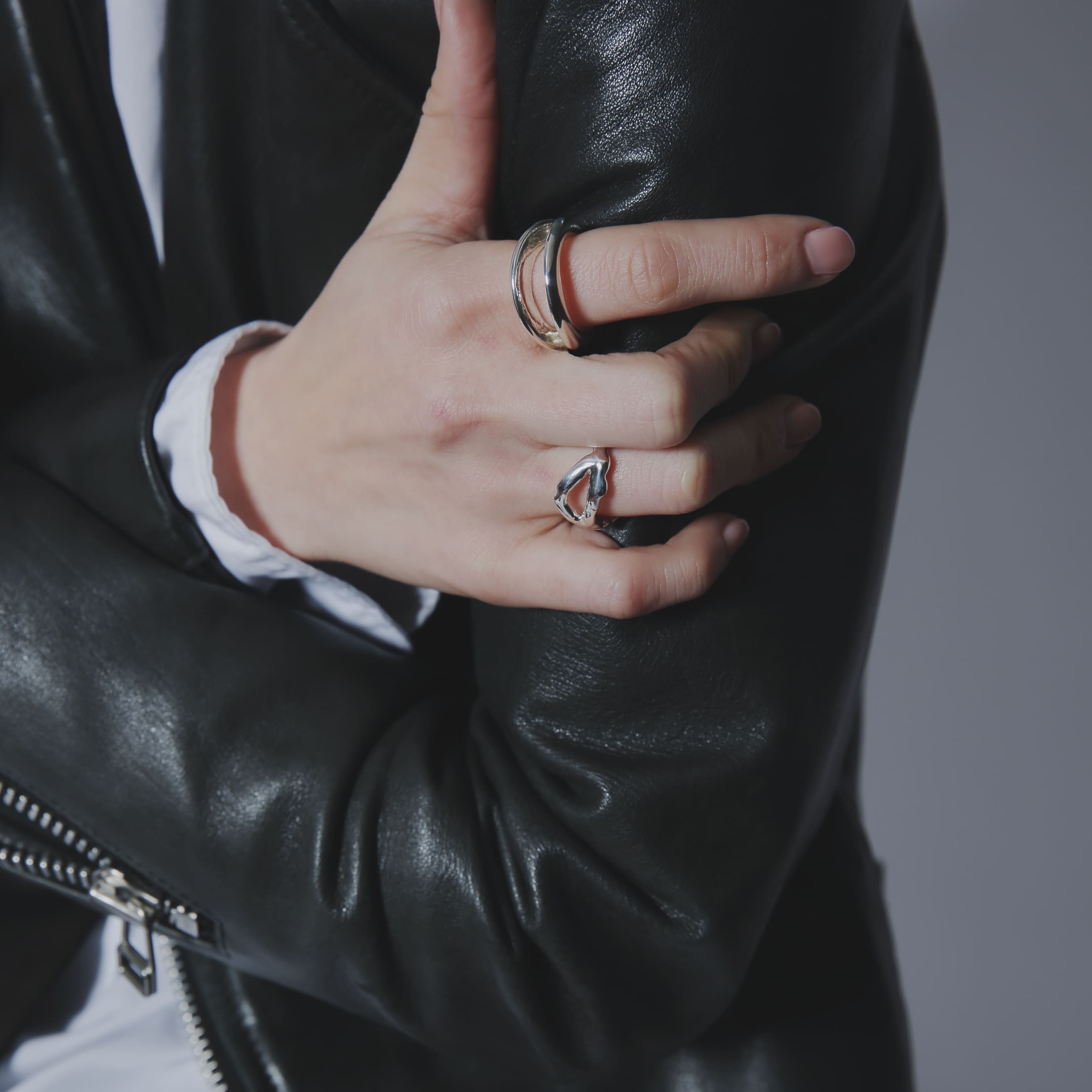黒のレザージャケットを羽織り、シルバー925製のリングを人差し指と薬指に重ね付けしたスタイリング。ハードな素材感にシルバーの光沢が映える手元のアップ。