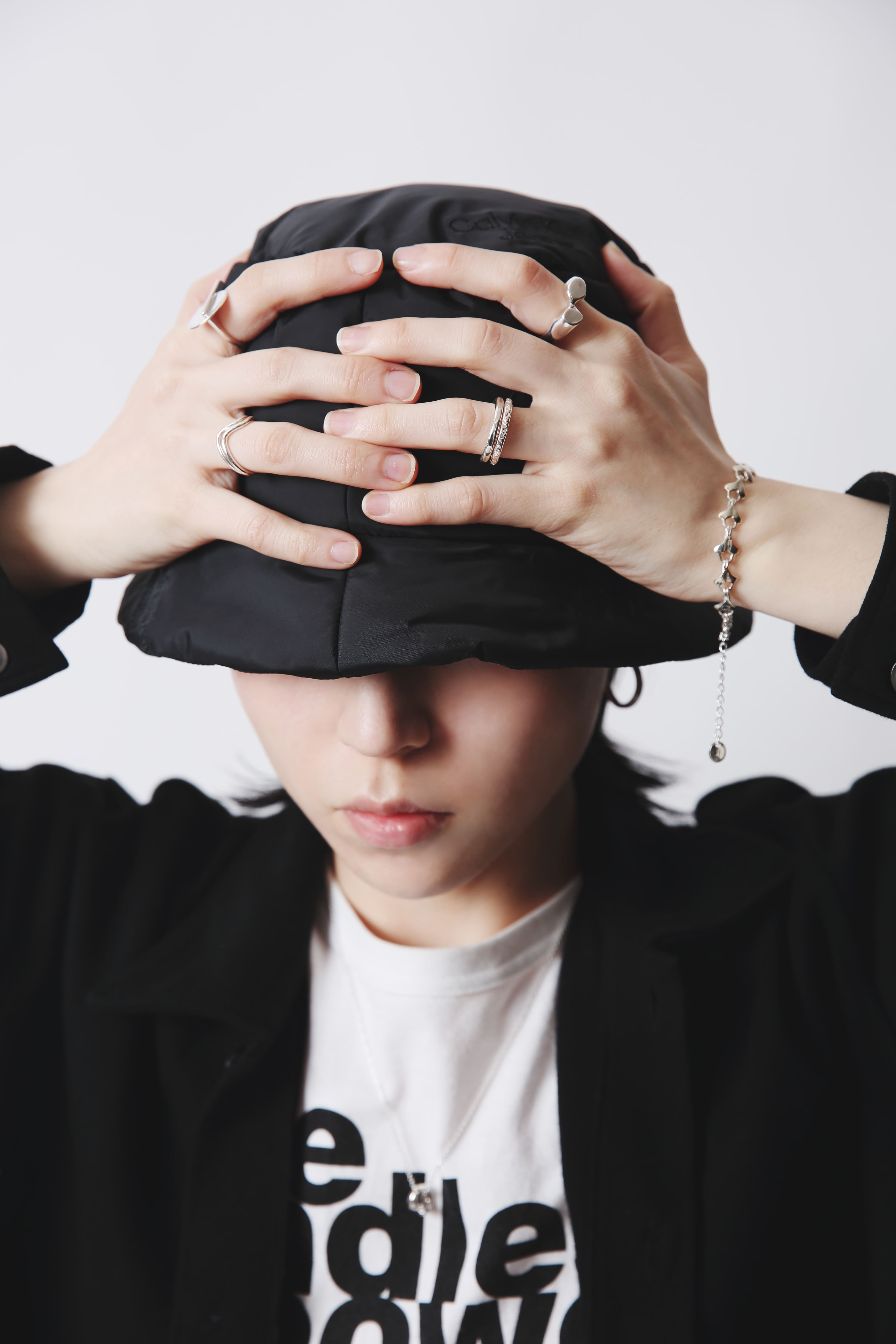 黒のバケットハットを両手で押さえるモデルの手元に、シルバー925製のイチョウの葉モチーフのブレスレットが輝く。個性的なリングとの重ねづけが印象的。