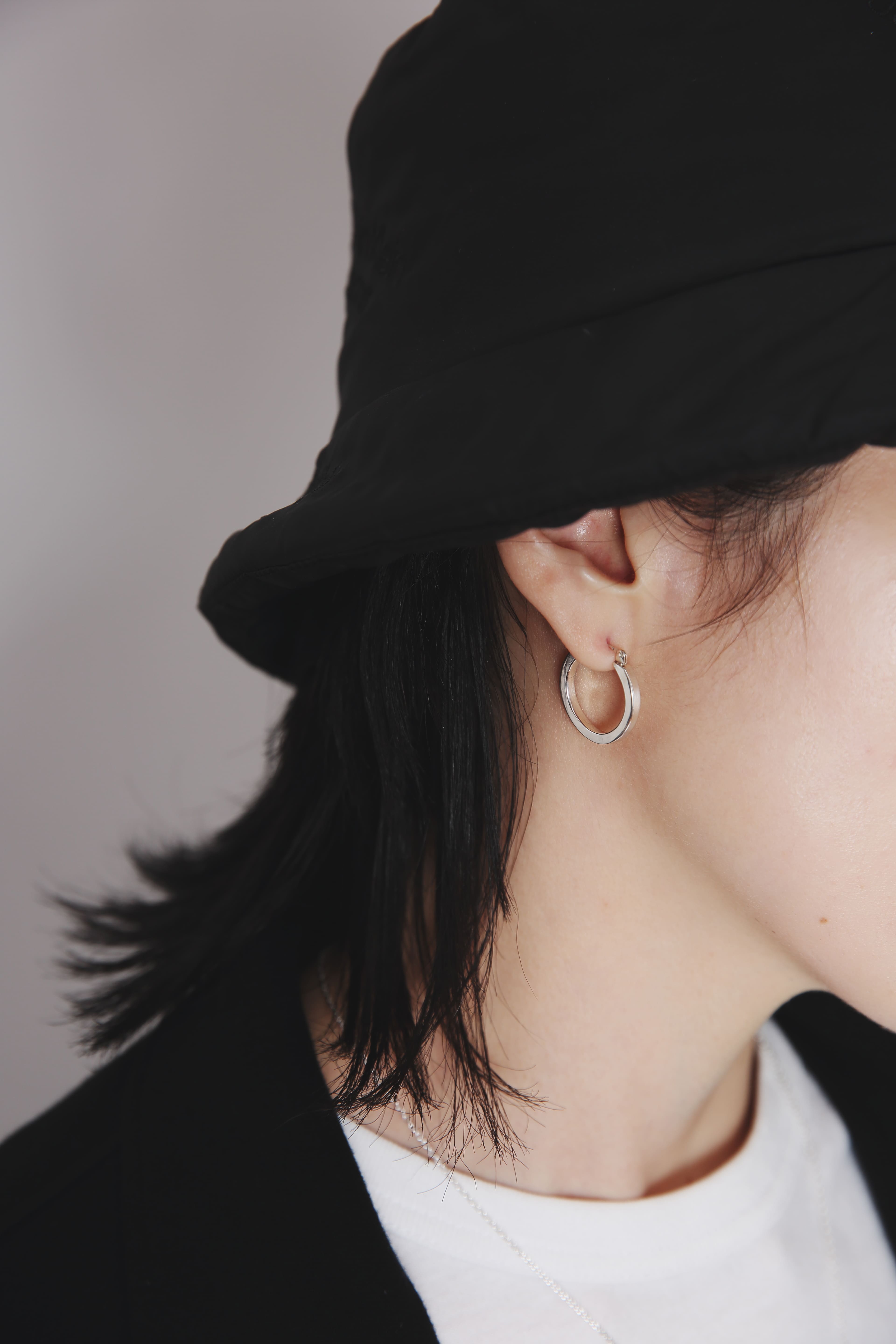 黒のバケットハットを被った人物が、耳元に直径21mmのシルバーフープピアスを着用しているクローズアップ写真。