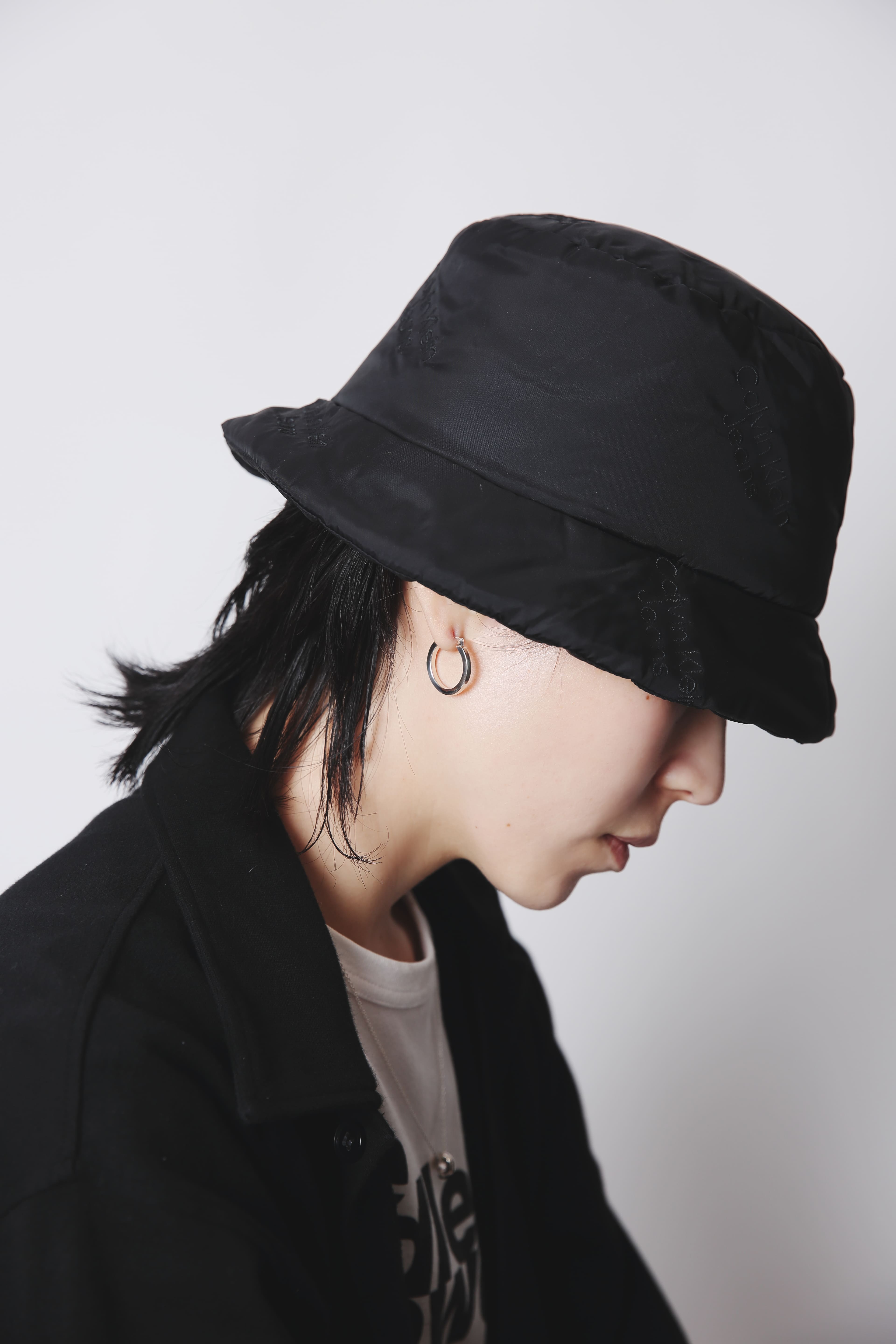 バケットハットとカジュアルな服装の人物が、斜め下を向いた状態でシルバーフープピアスを着用している様子。
