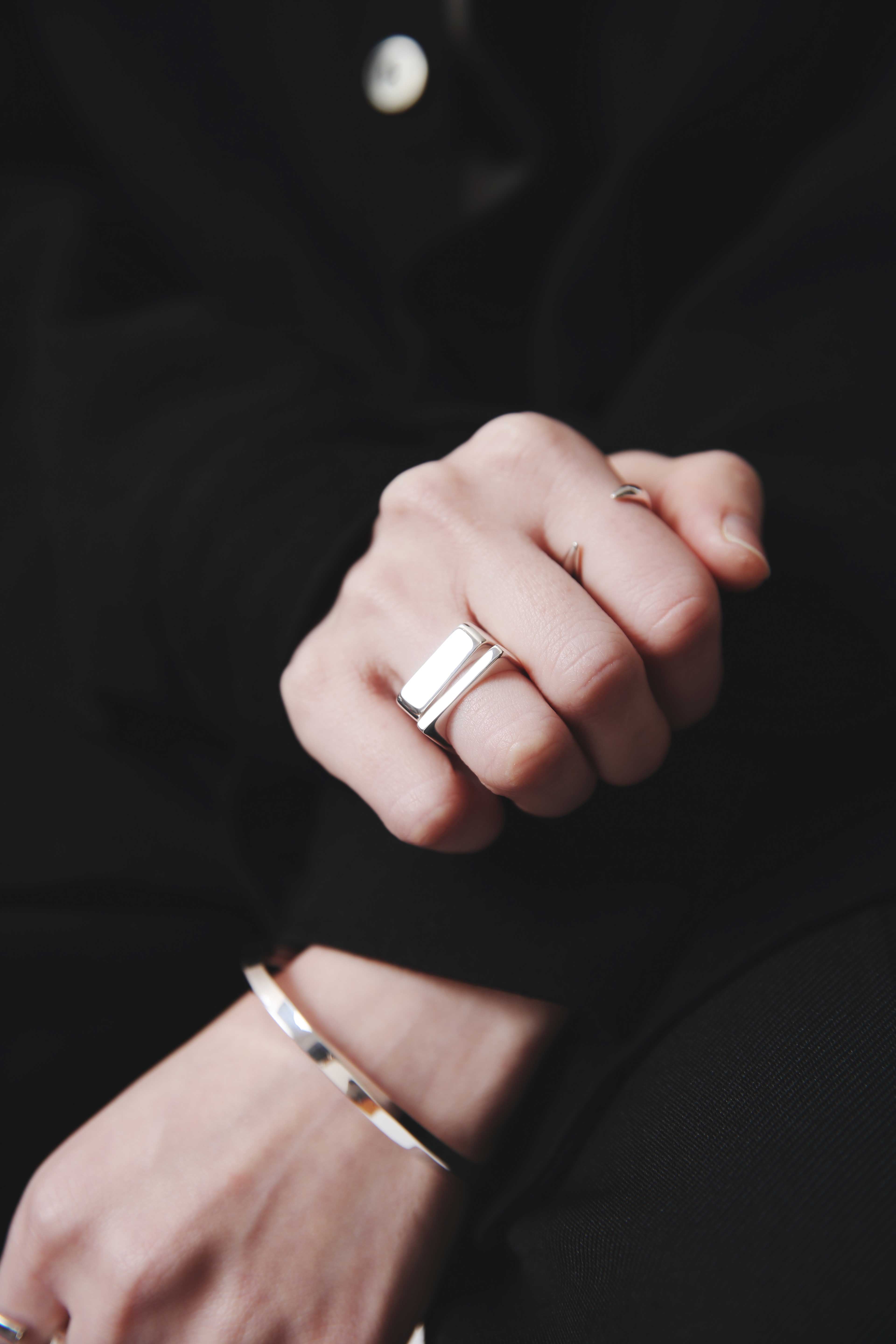シルバーのバングルと幅広デザインのシルバーリングを着けた手元。ブラックコーデに映えるミニマルで上品なジュエリースタイリング。