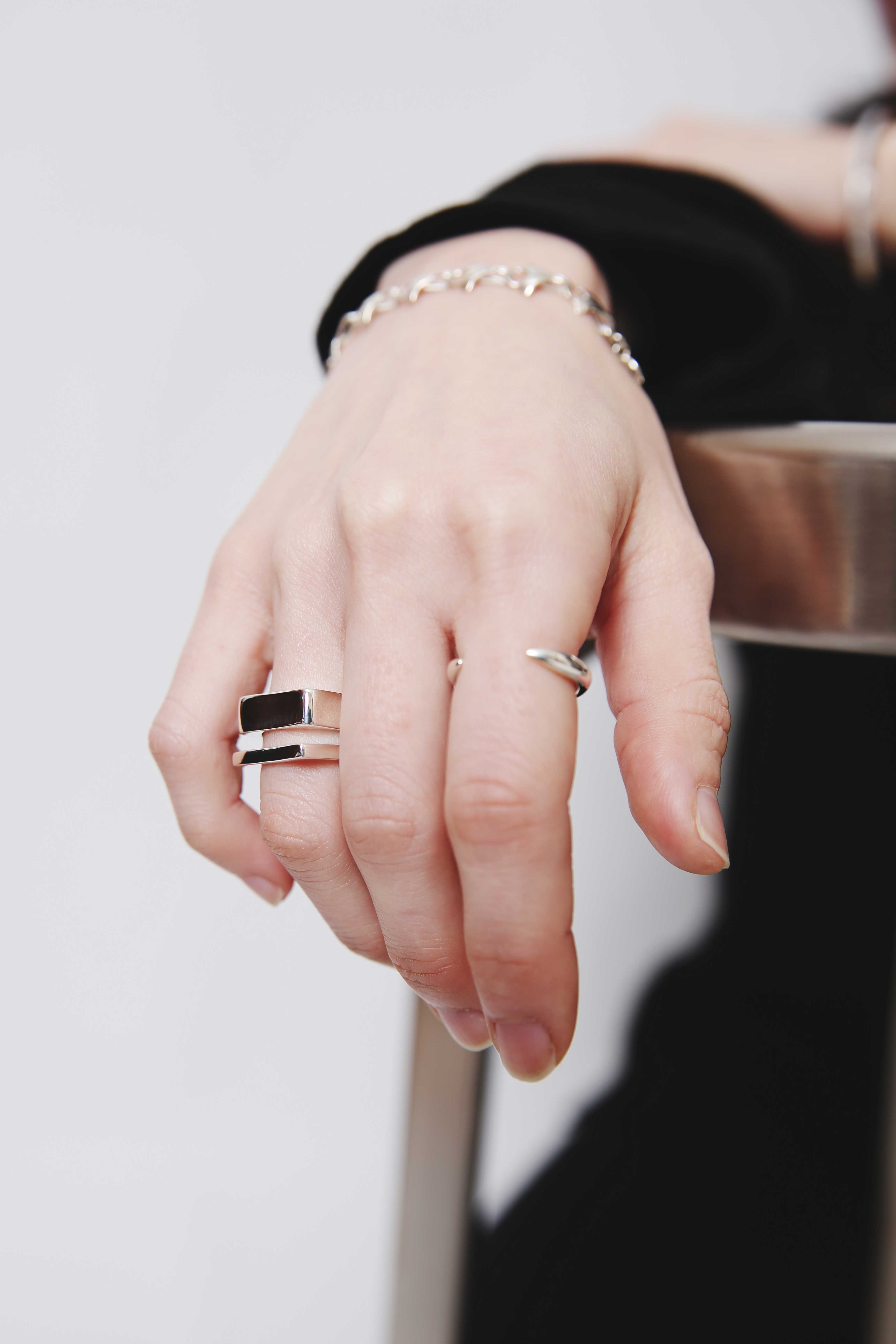 Nine Nineのシルバー925スクエアリングとカーブオープンリング、ブレスレットで椅子に手を添えたモードスタイル