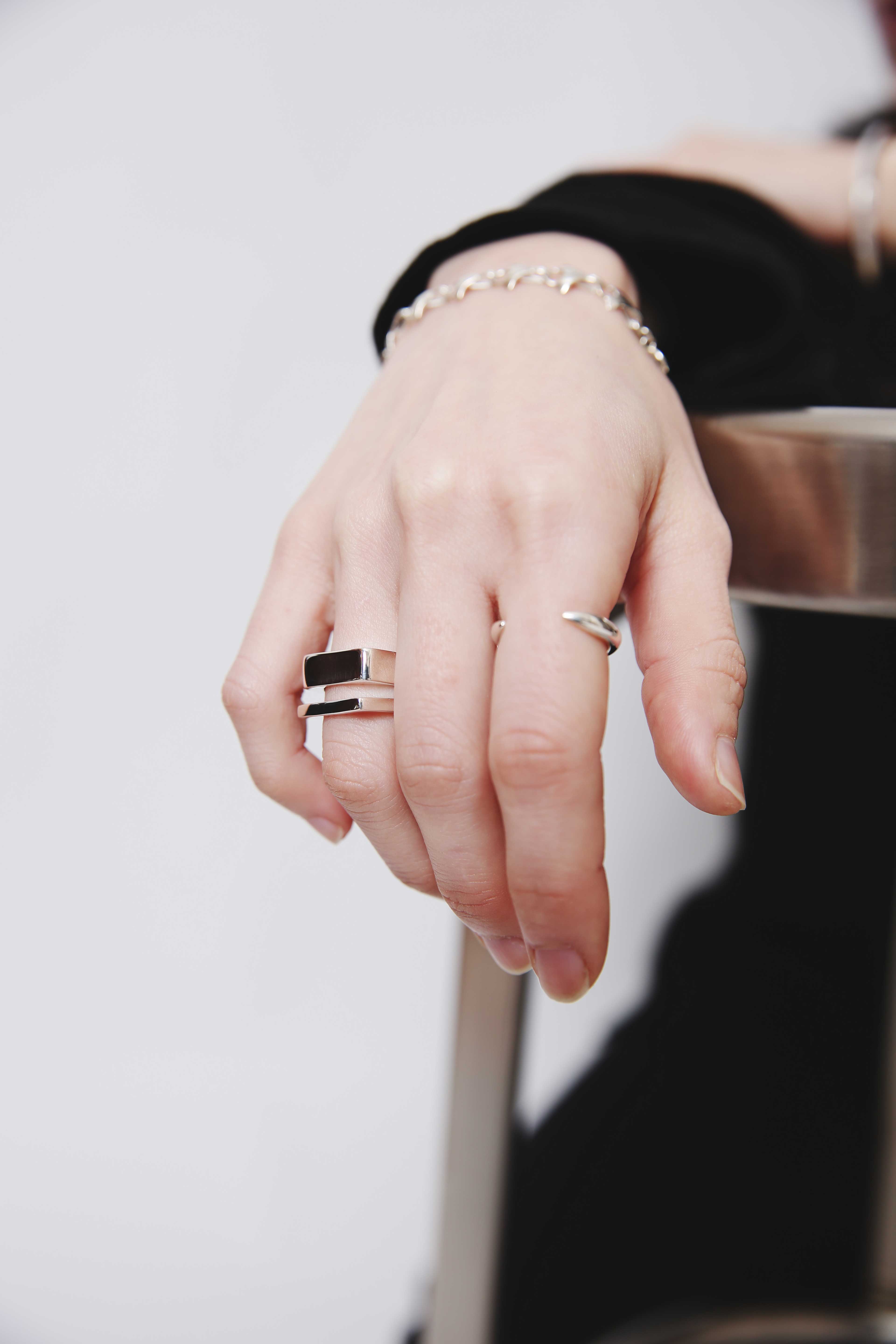シルバーチェーンブレスレットと2本のシルバーリングを重ね付けした手元のアップ写真。ミニマルなブラックコーデとシンプルなアクセサリーのスタイリング。