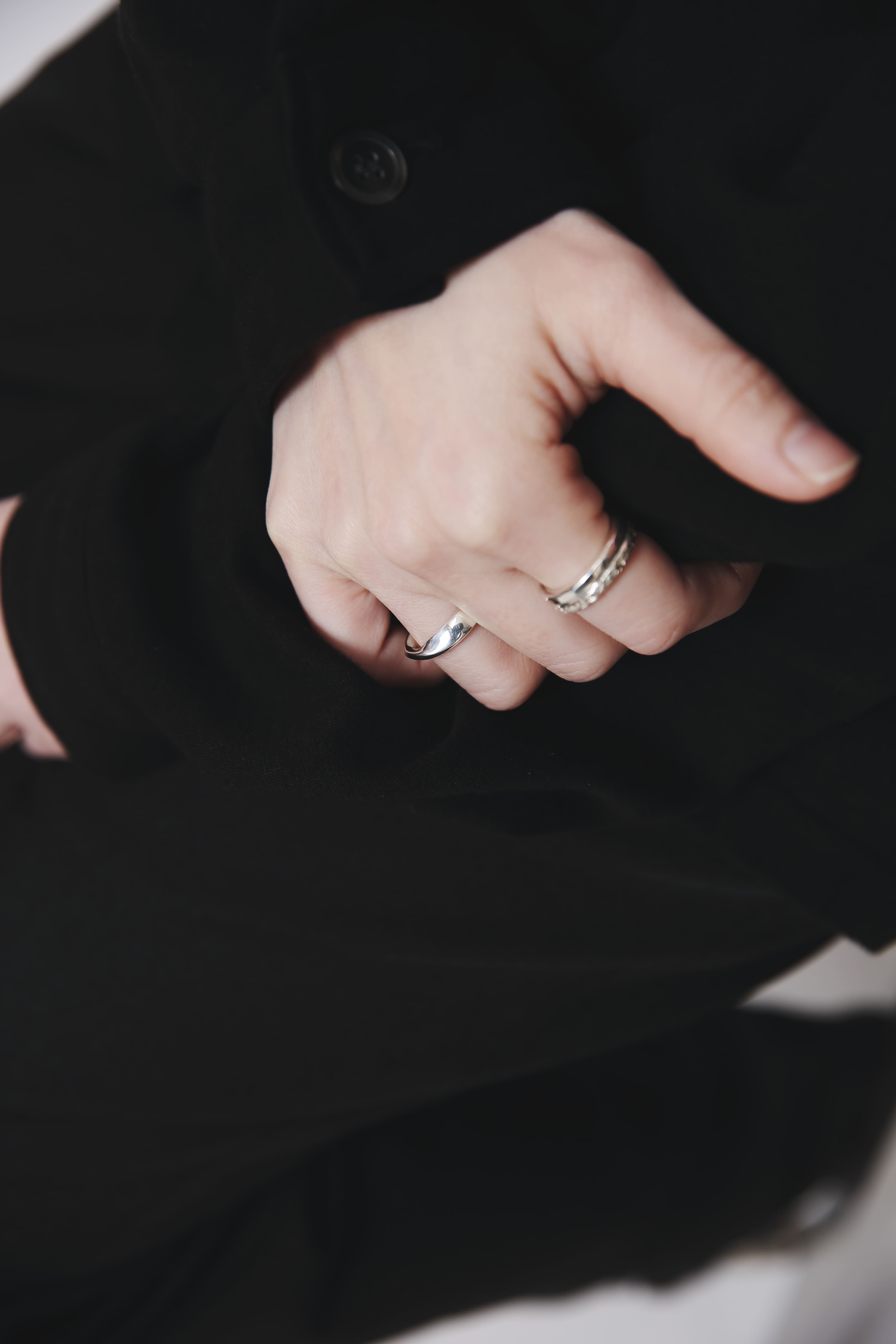 黒い袖口に手を添える手元のクローズアップ。薬指にプレーンなシルバーリング、人差し指い重ね付けリングを着用。