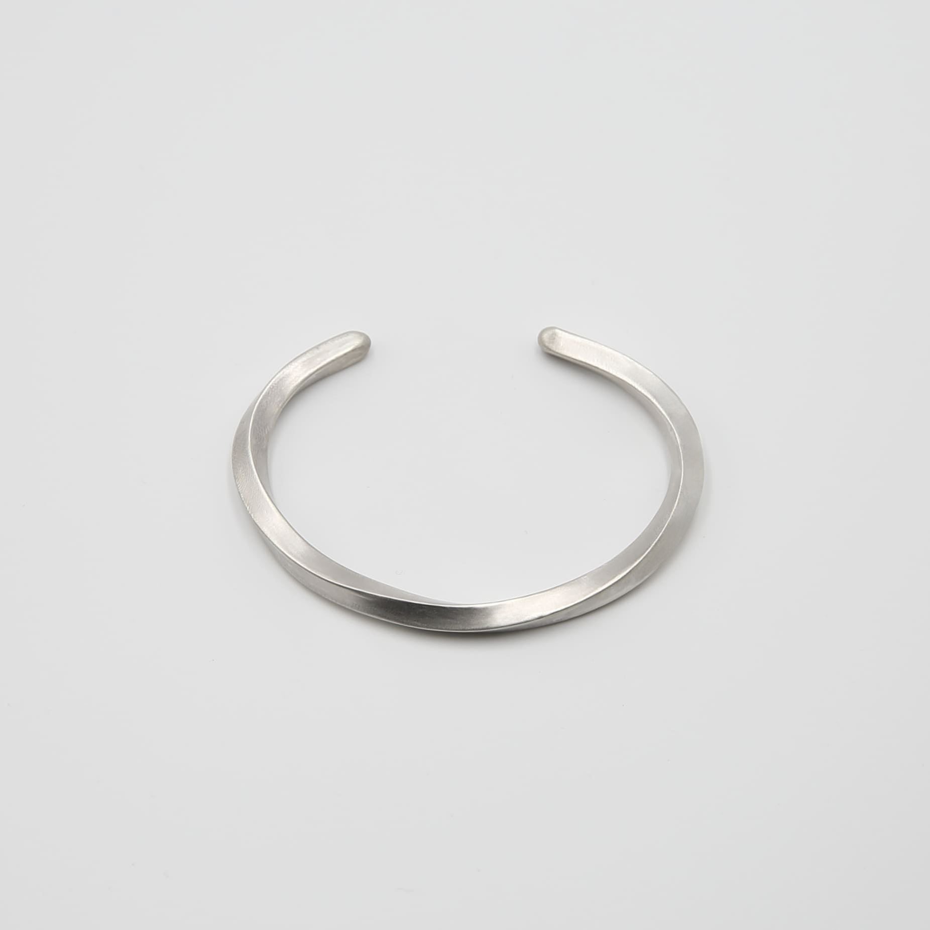 シルバー925製のシンプルなバングル。流れるような曲線が特徴のデザインで、マットな質感が落ち着いた印象を与える。