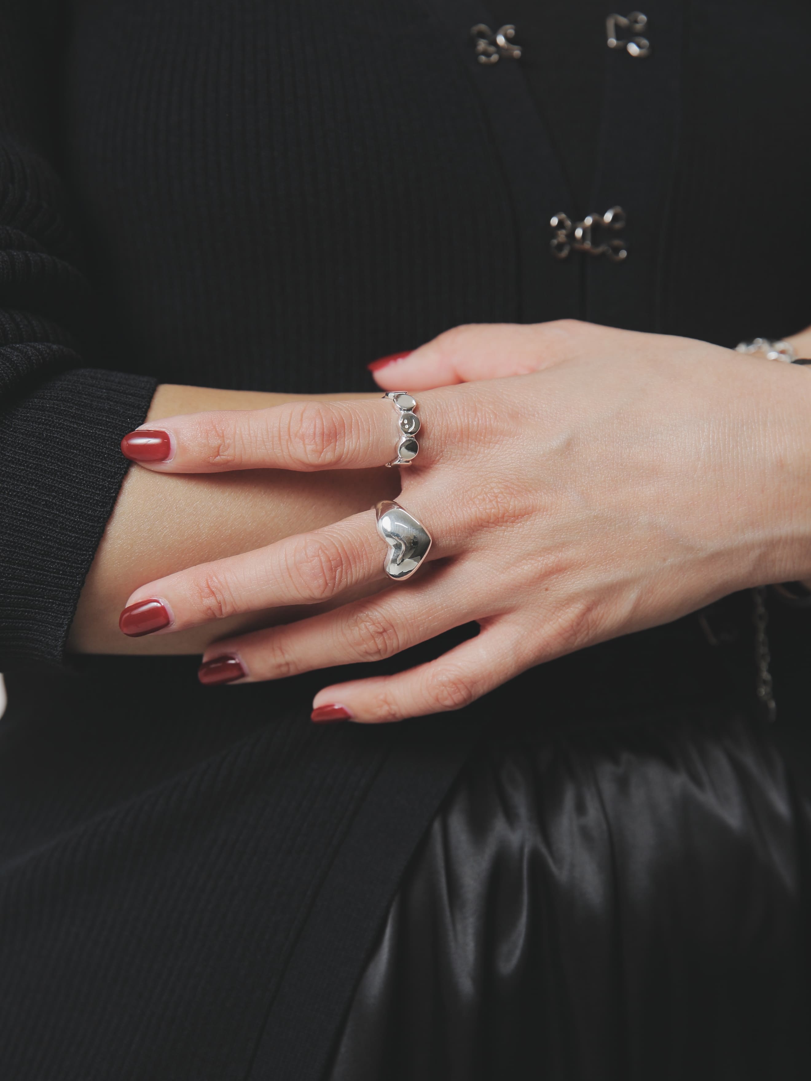 腕を組んだポーズで、シルバー925のアクセサリーが黒い衣装に映えるカット。大ぶりなハートリングがアイコニックな存在感を放ち、手首のバングルとともに洗練された印象を与えます。