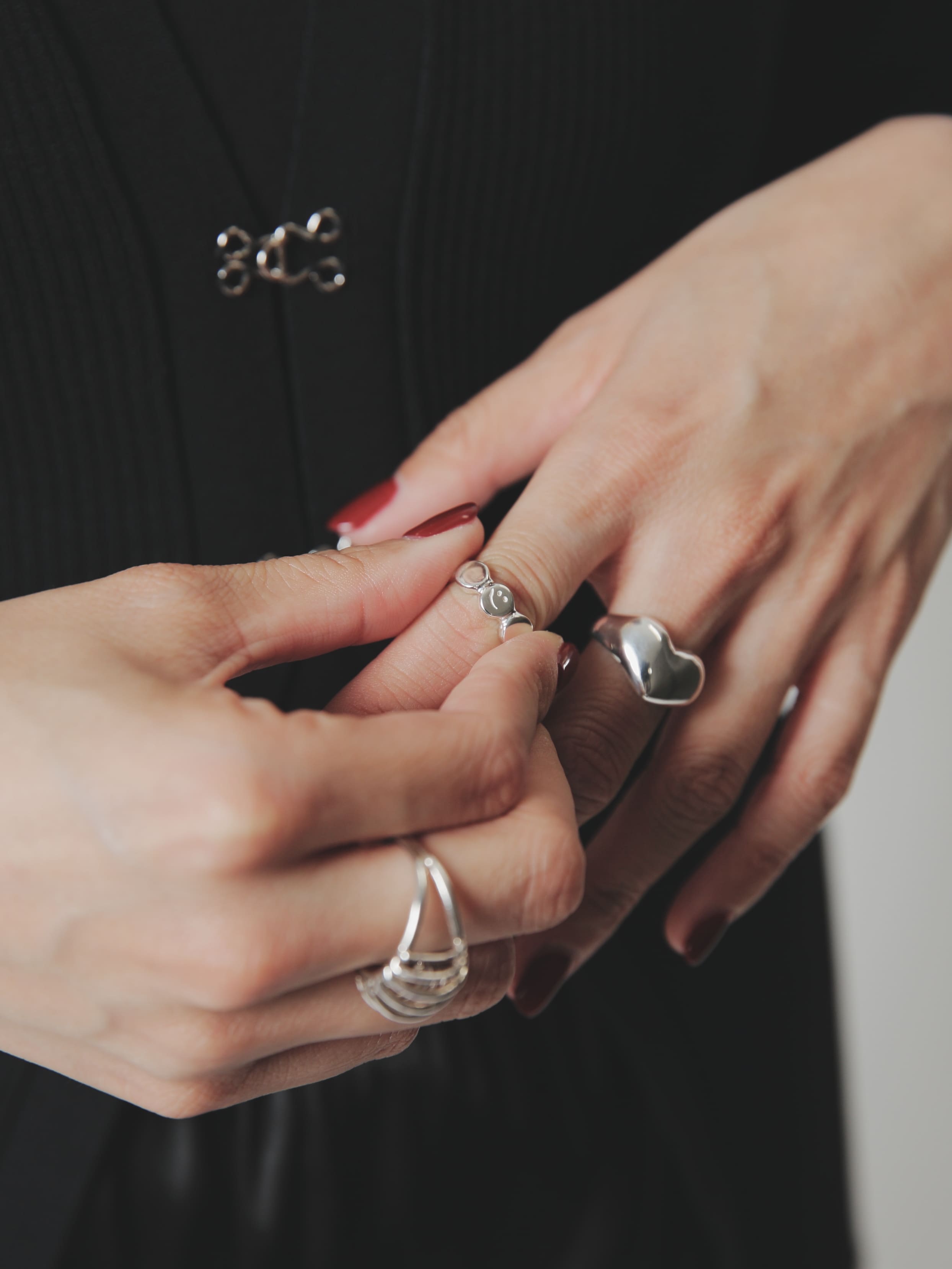黒コーデの手元をクローズアップ。ボルドー系ネイルに、ハートモチーフリング、にこちゃんマークモチーフリング、を重ね付けしたシルバー925ジュエリーのスタイリング