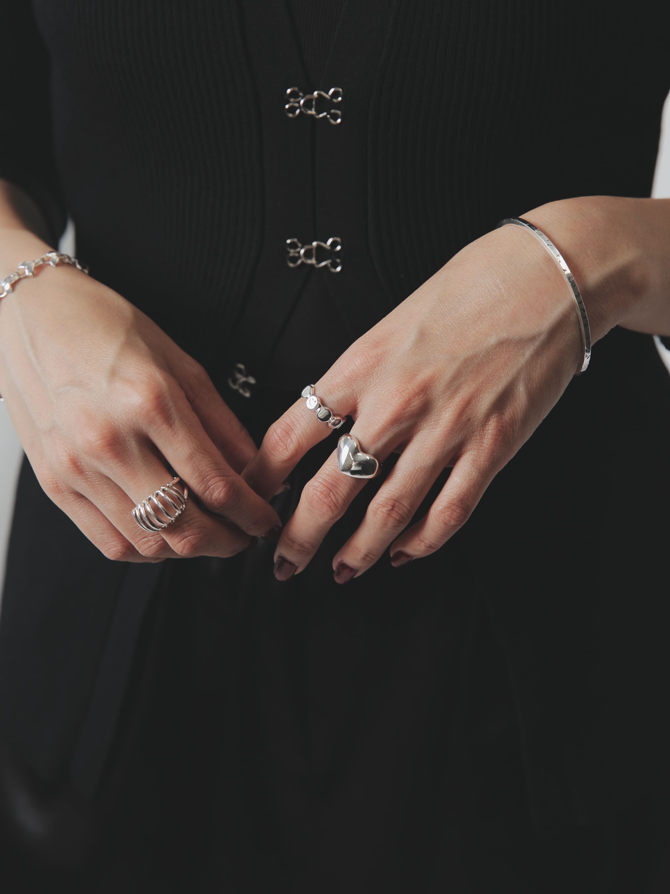 黒のトップスにボルドーネイルが映える手元。シルバー925製のハートモチーフリングと丸パーツが連なるリングを重ね付けした上品なジュエリースタイリング。