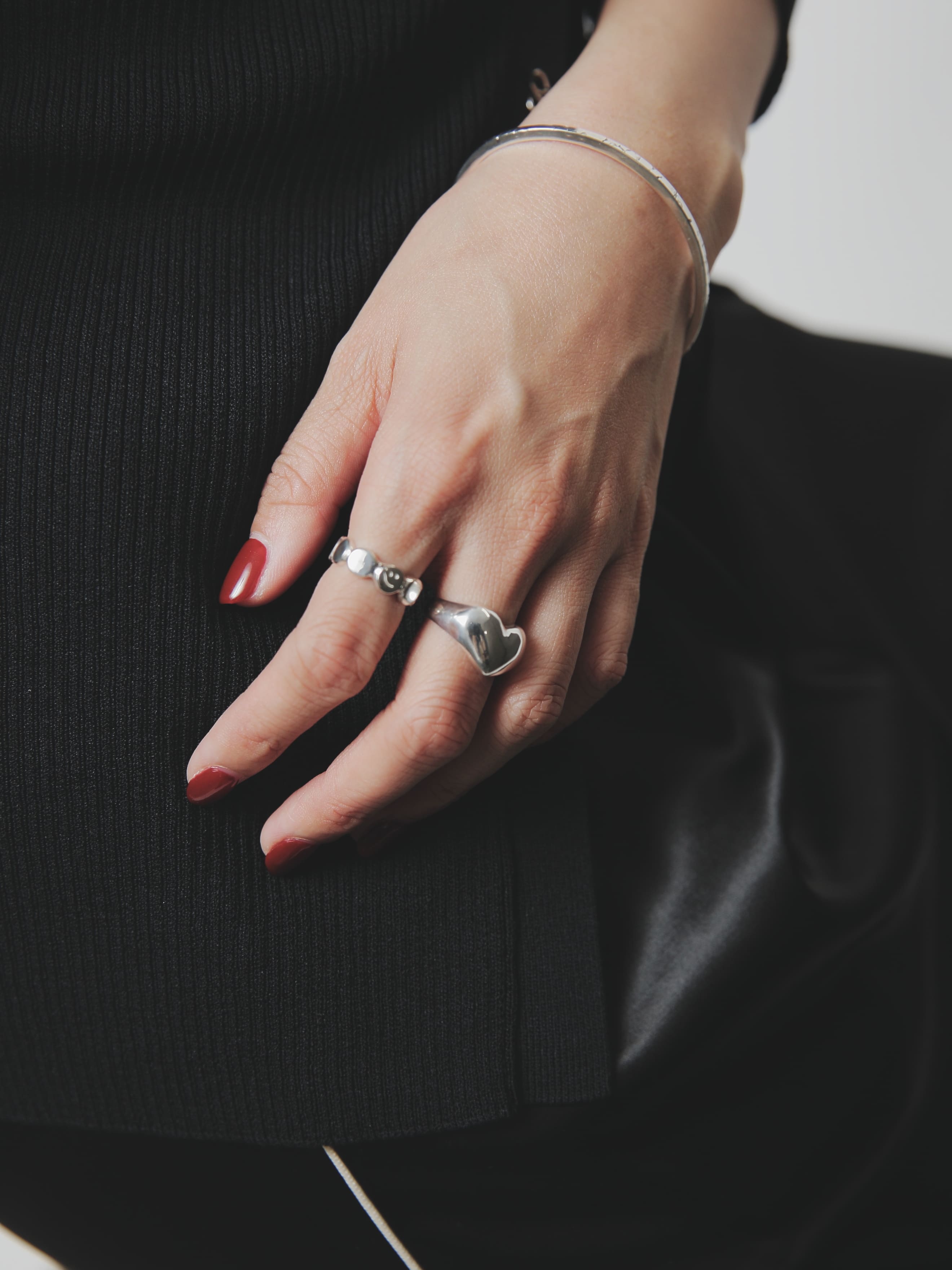 細身のバングルと立体感のあるシルバー925リングを重ねたナチュラルな手元ショット。黒のトップスとのコントラストが美しい構図。