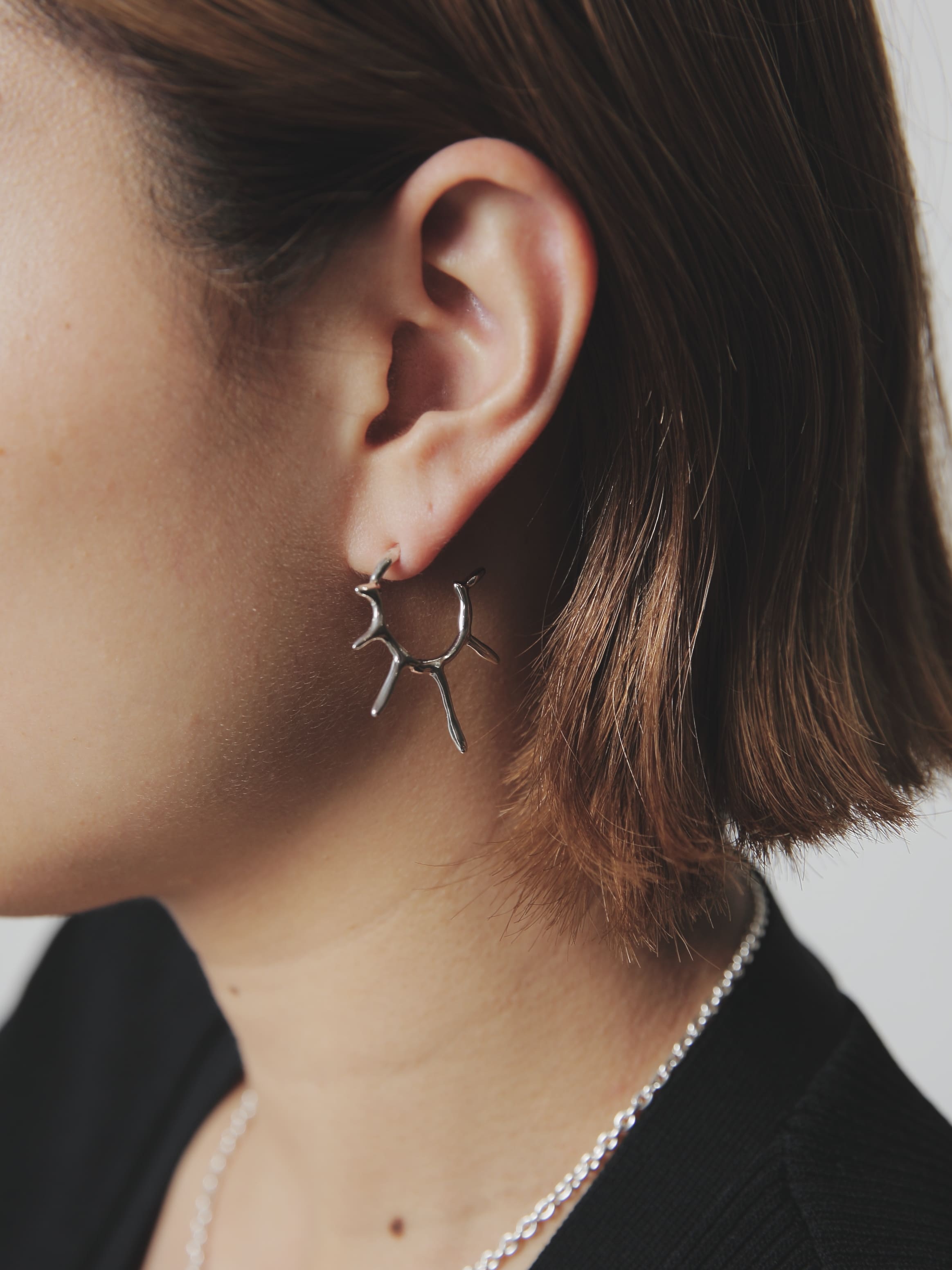 枝のようなフォルムが特徴的なシルバー925製フープピアスを着用した横顔ショット。独創的で立体的なデザインが耳元にアクセントを加える。