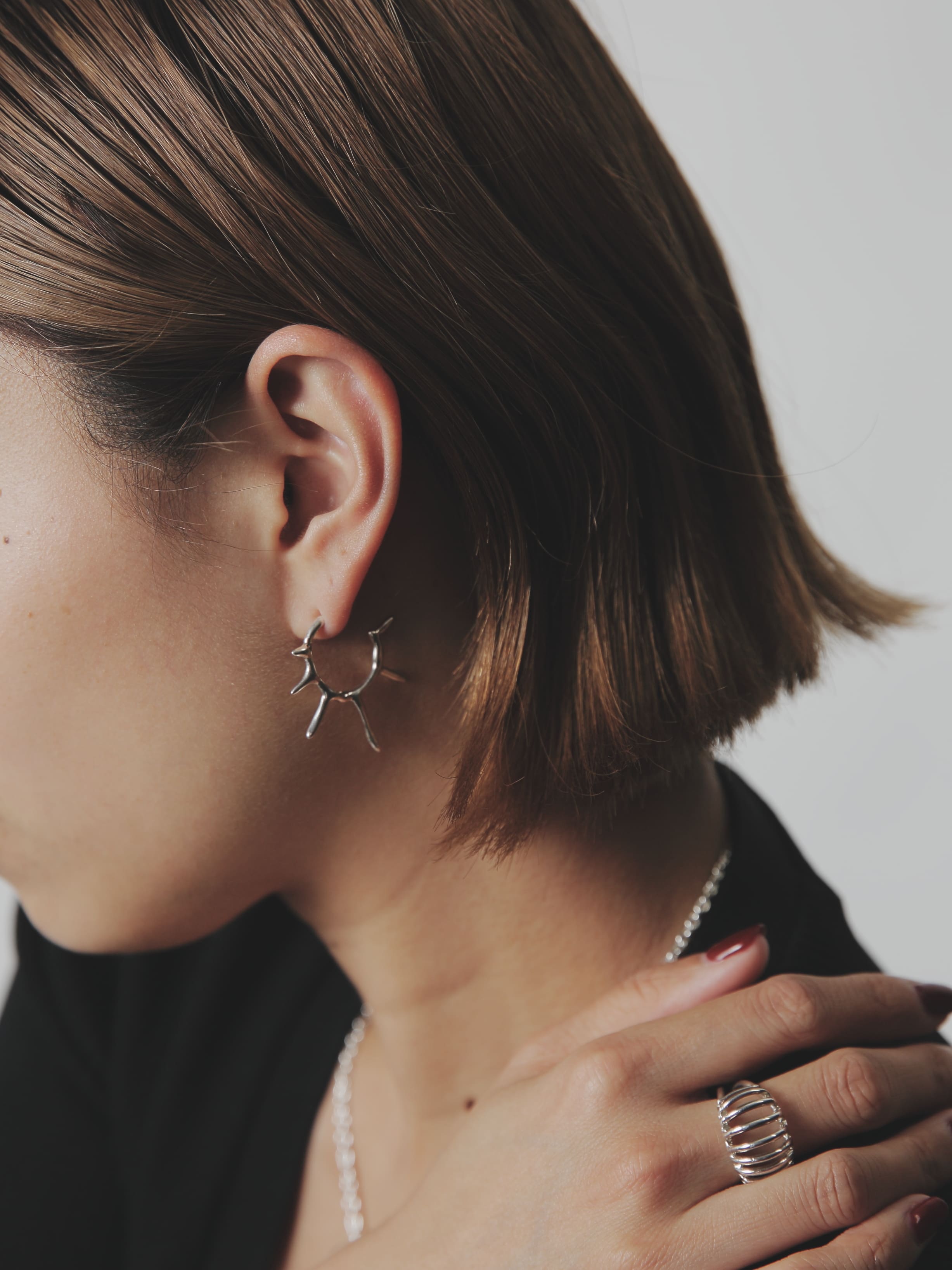 ユニークな造形のシルバー925ピアスとワイドフォルムのシルバーリングを組み合わせた洗練スタイル。ショートボブとモノトーンコーデに映えるアクセサリー使い。