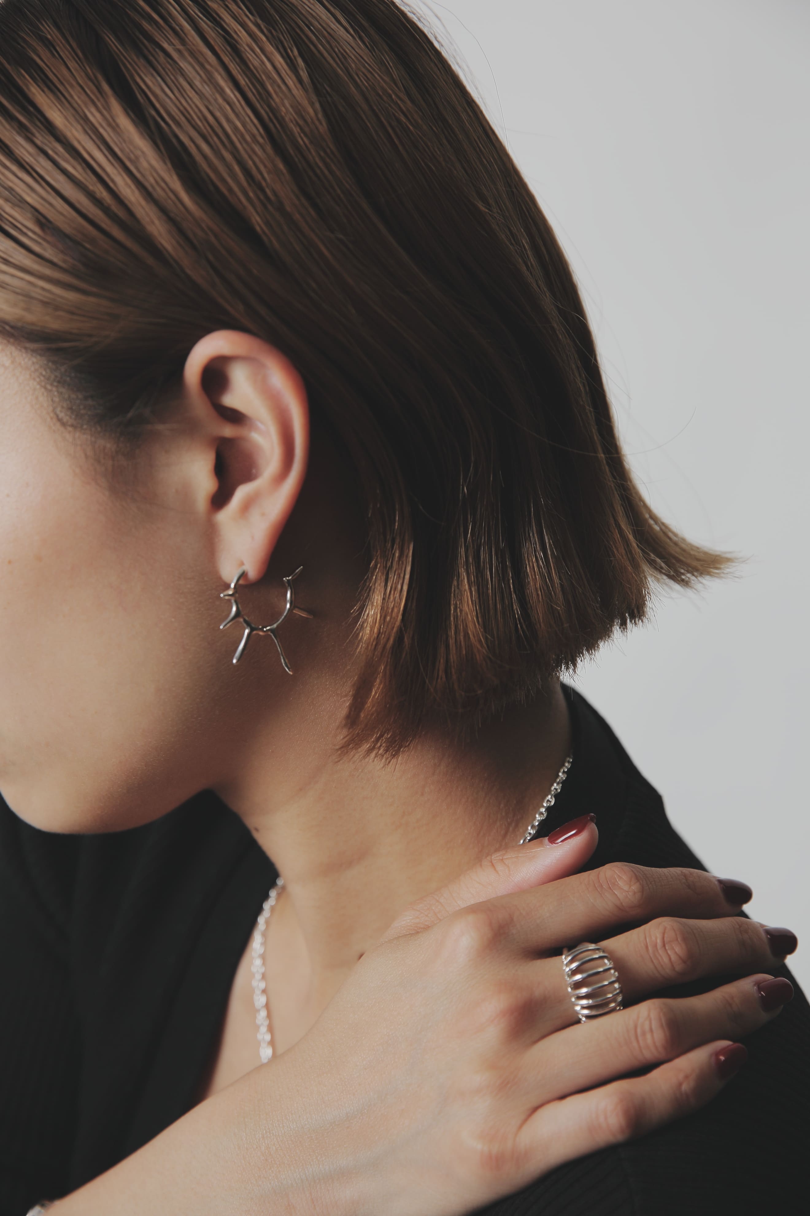 女性の耳元のピアスと、指に着けたシルバーリングのコーディネート。洗練されたシルバージュエリーがモノトーンコーデに映える。
