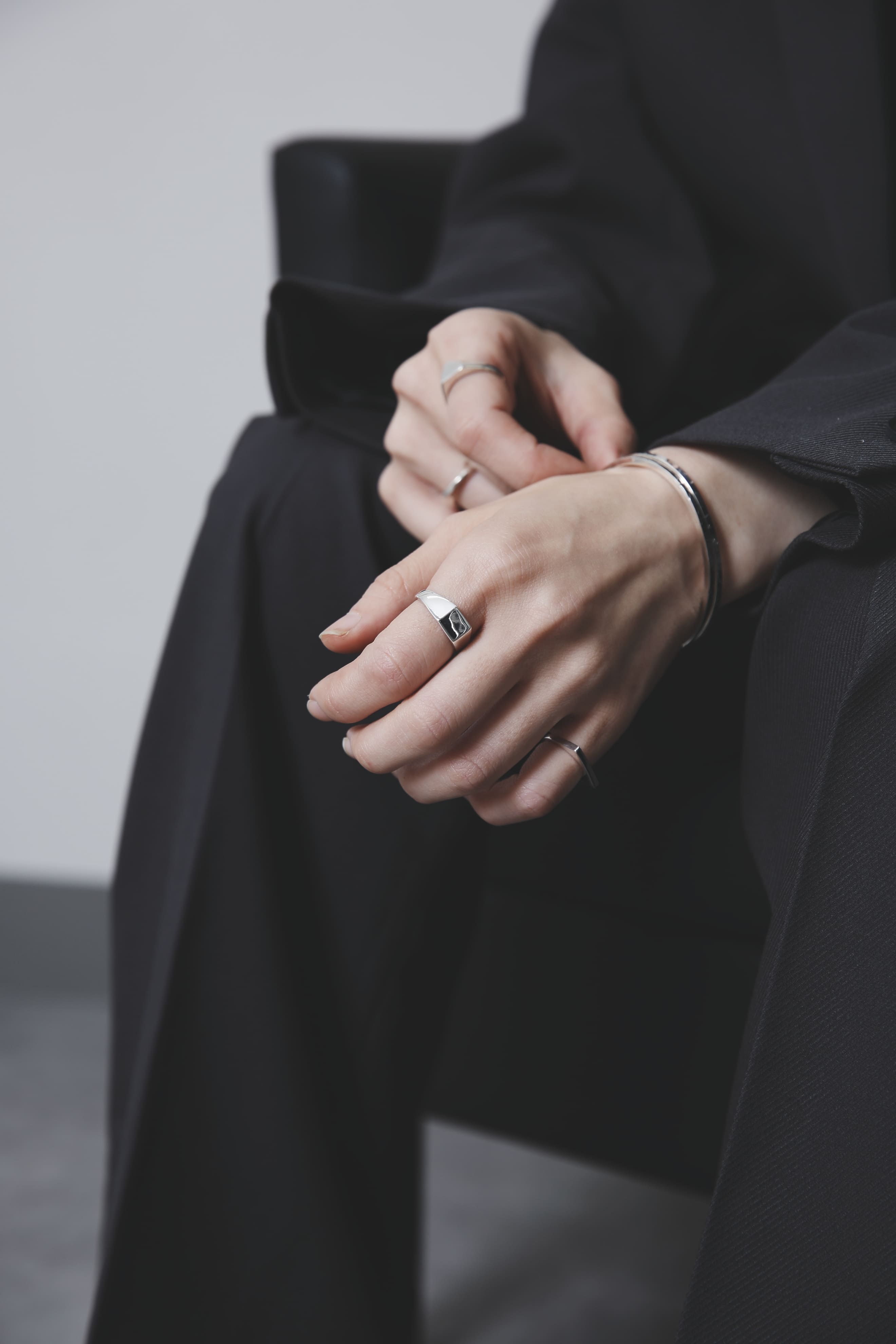 黒いセットアップに合わせた手元のカット。角を落としたスクエア型のシルバーシグネットリングが存在感を放ち、他のリングやバングルとのレイヤードで奥行きを演出。