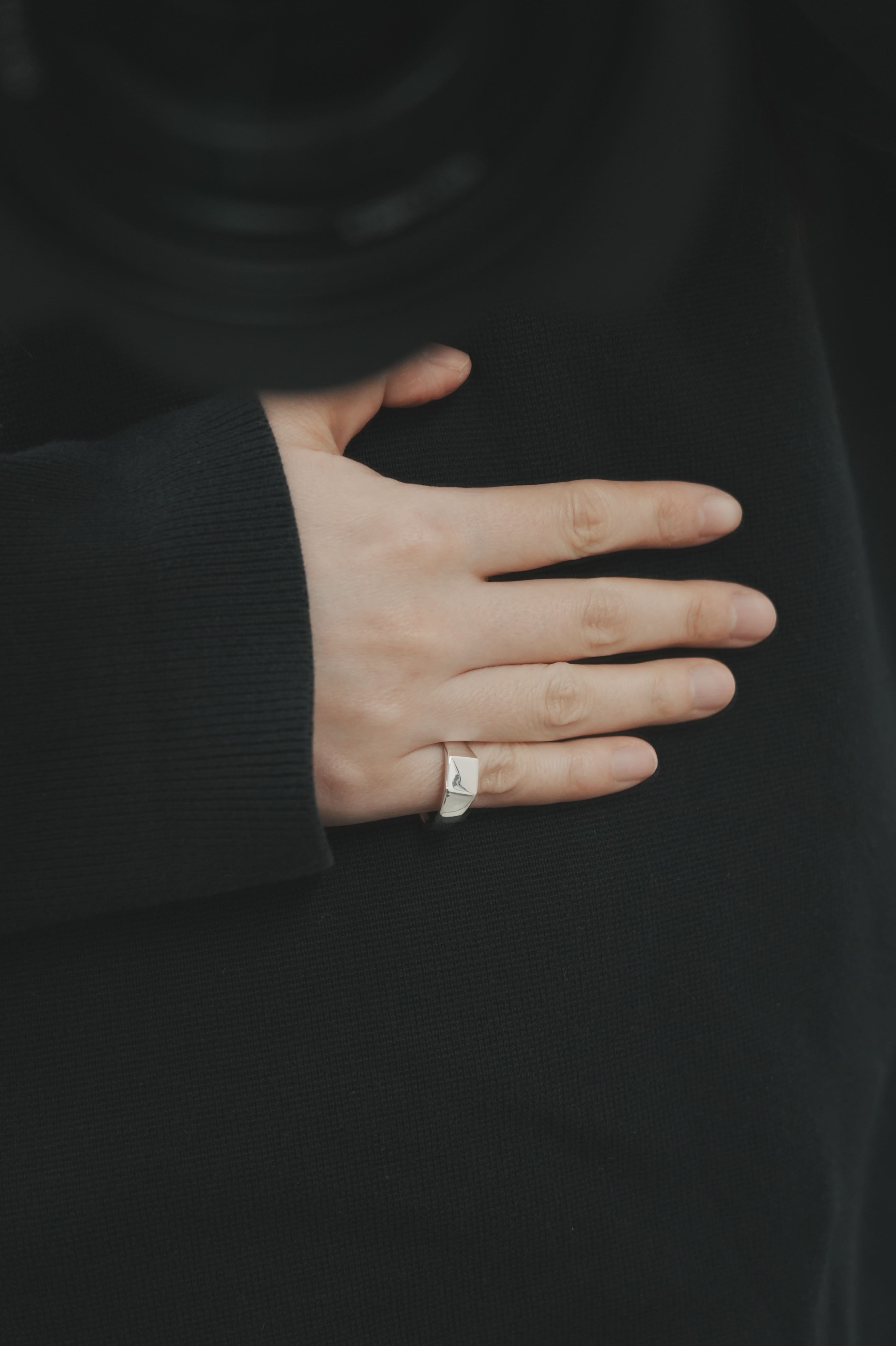 黒いトップスの袖口から覗く手元に、台形フォルムのシルバーシグネットリングを着用。無駄のないデザインが、落ち着いたスタイルの中で静かに輝きを放つ。