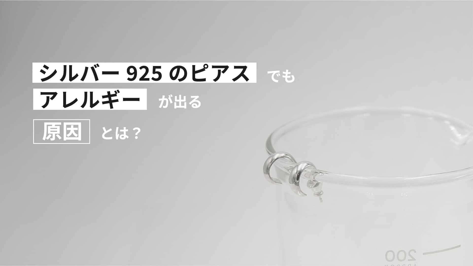 「シルバー925のピアスでもアレルギーが出る原因とは？」という文字がデザインされた画像。透明なガラス容器の縁にシルバーのピアスが掛けられている。