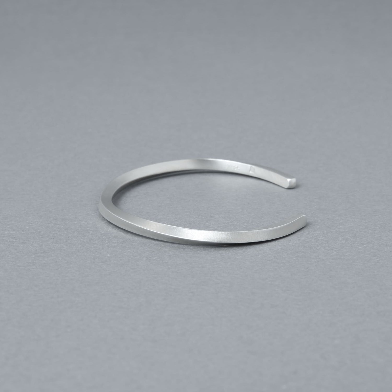 やや斜め上から捉えたシルバーバングルのディテール写真。落ち着いたヘアライン仕上げと滑らかな曲線が際立つ。