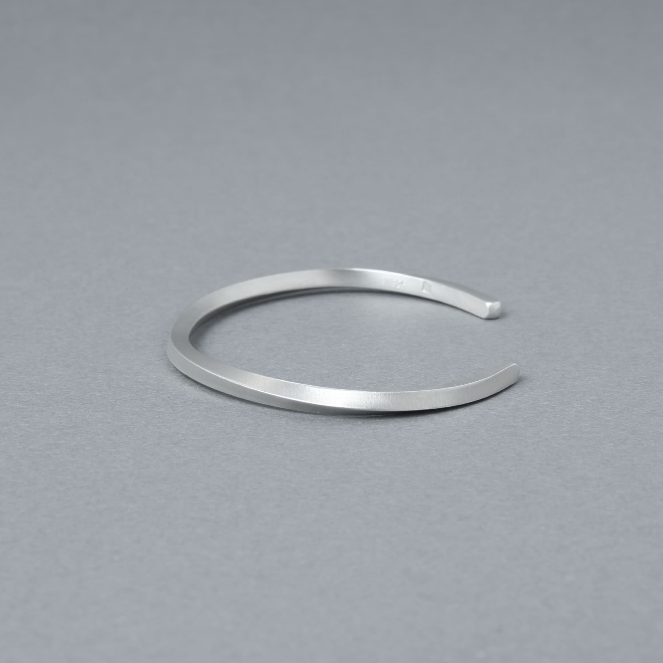 やや斜め上から捉えたシルバーバングルのディテール写真。落ち着いたヘアライン仕上げと滑らかな曲線が際立つ。