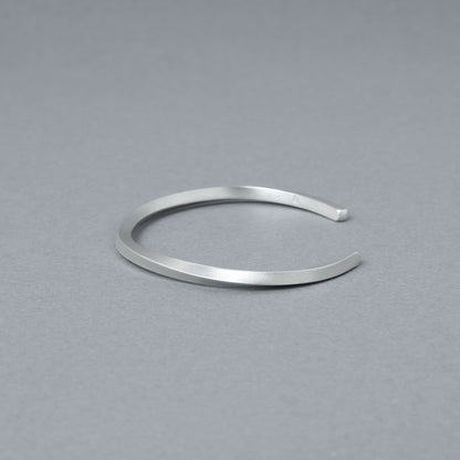 やや斜め上から捉えたシルバーバングルのディテール写真。落ち着いたヘアライン仕上げと滑らかな曲線が際立つ。