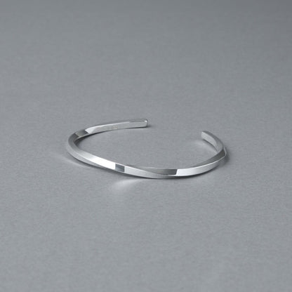 シルバー925バングル「21-B-005」（幅3mm）を、開口部を奥に向けてグレー背景で撮影。ねじりのあるフォルムと鏡面仕上げの輝き、内側の刻印が見える商品写真。周囲に余白を残した構図。