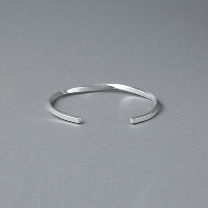 シルバー925バングル「21-B-005」（幅3mm）を、開口部を手前にしてグレー背景で撮影。ねじりのあるフォルムと鏡面仕上げの輝き、両端の形状が見える商品写真。