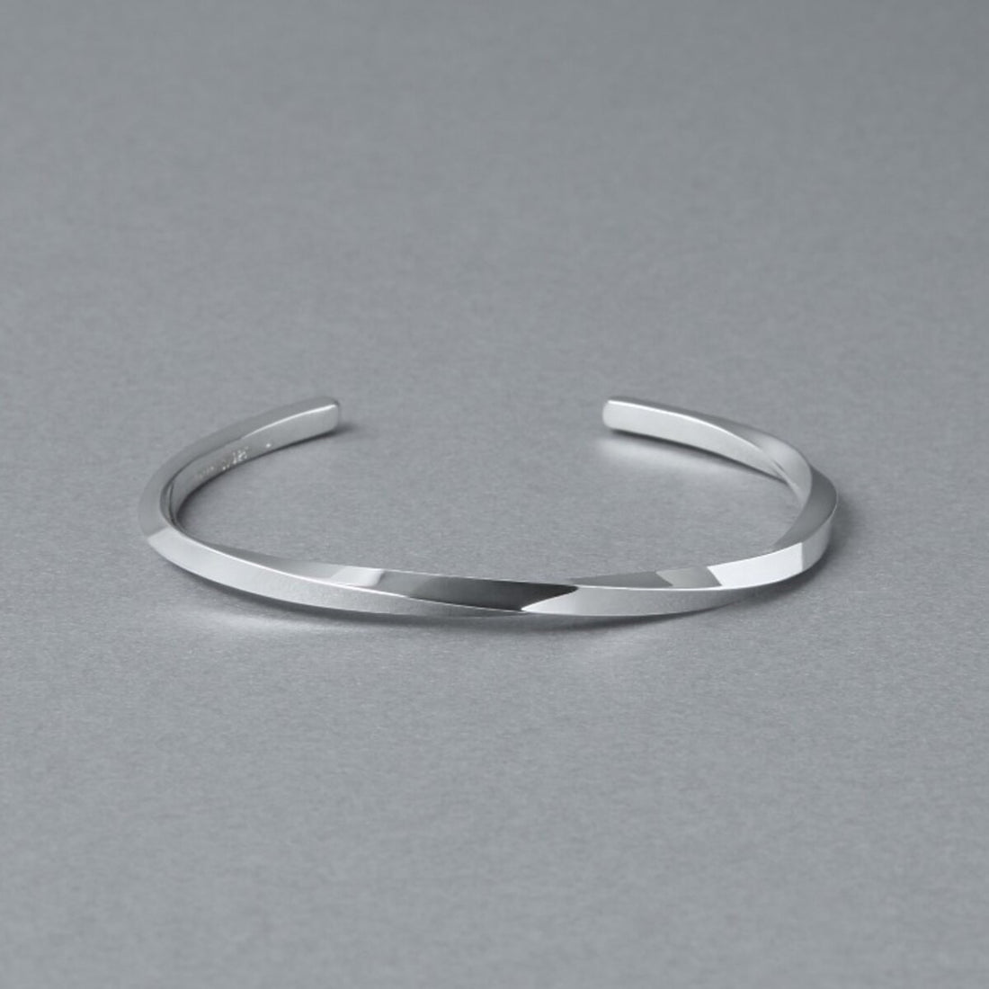 シルバー925バングル「21-B-005」（幅3mm）の商品写真。ねじりのあるフォルムと鏡面仕上げの輝き、開口部をグレー背景で斜め上から撮影。