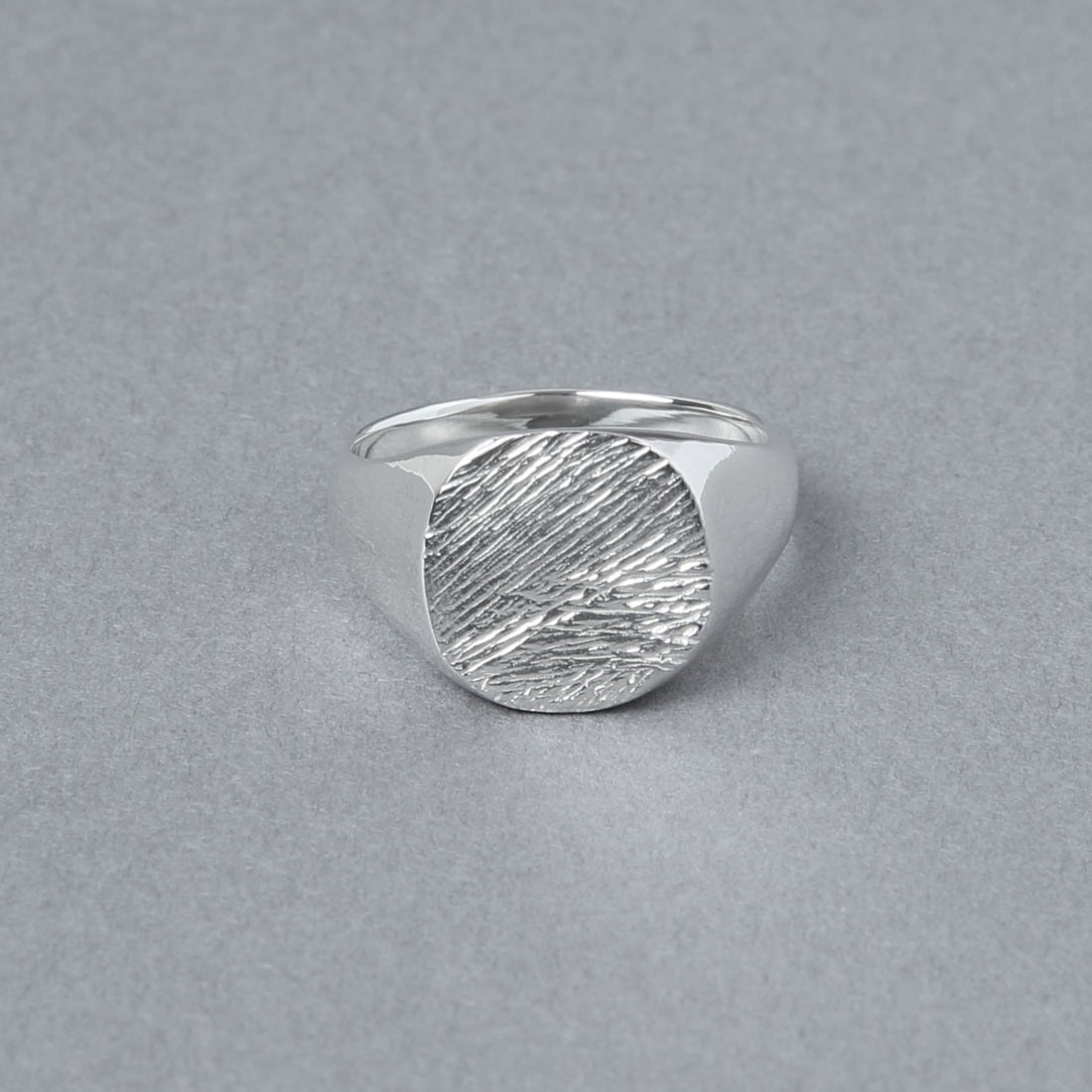 グレーの背景上に置かれた、丸いトップに繊細な木目模様が刻まれたシルバー925リング。立体的な陰影が素材の輝きを引き立てている。