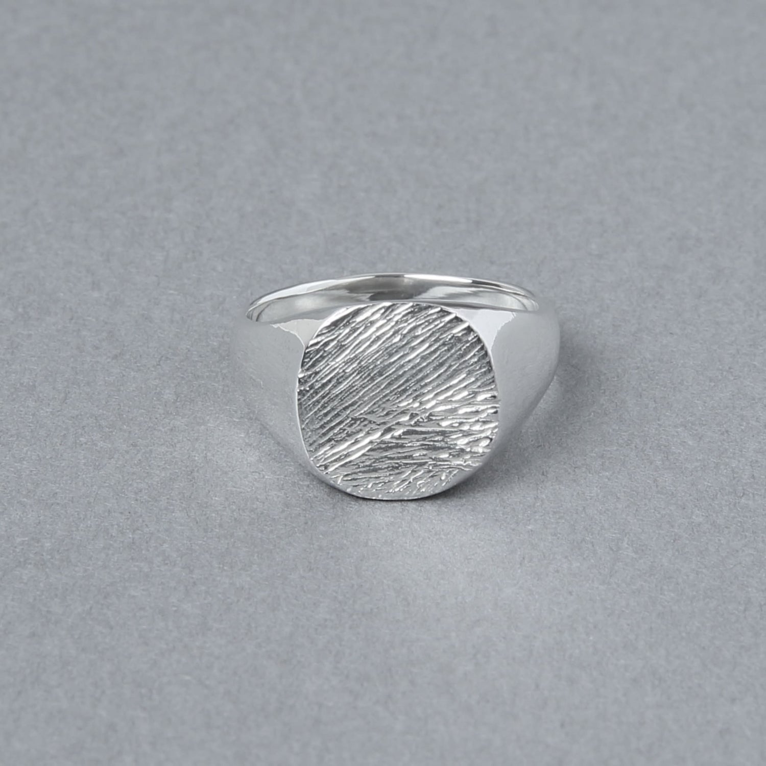 グレーの背景上に置かれた、丸いトップに繊細な木目模様が刻まれたシルバー925リング。立体的な陰影が素材の輝きを引き立てている。