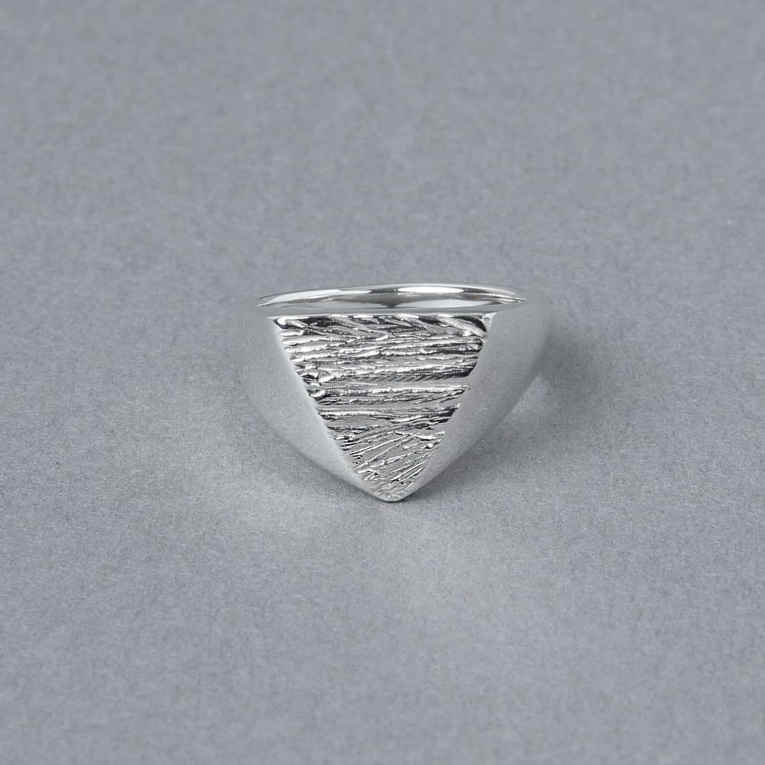 三角形のトップに木目のようなテクスチャが施されたシルバー925シグネットリング。正面から見た写真で、エッジの効いたフォルムが印象的。