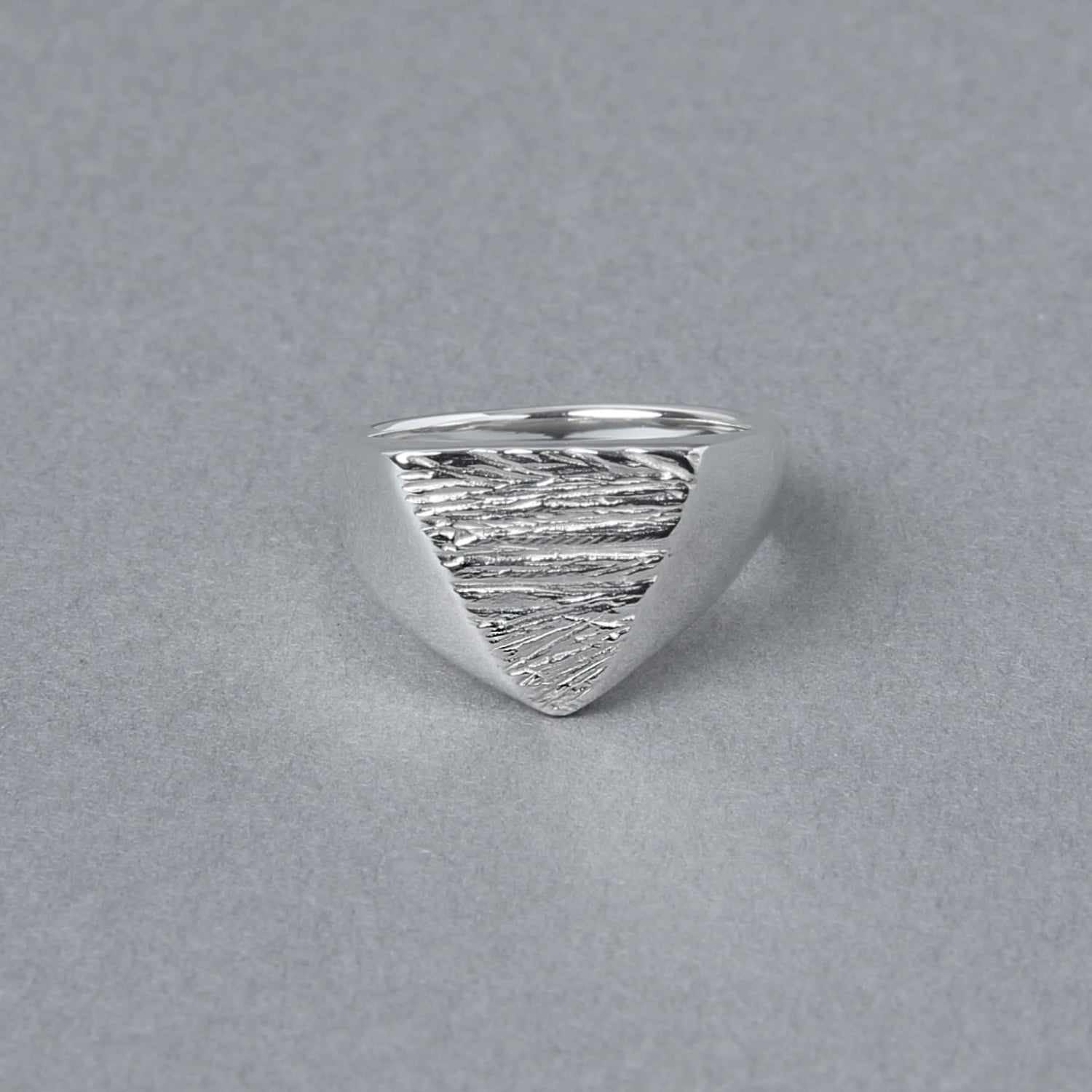 三角形のトップに木目のようなテクスチャが施されたシルバー925シグネットリング。正面から見た写真で、エッジの効いたフォルムが印象的。