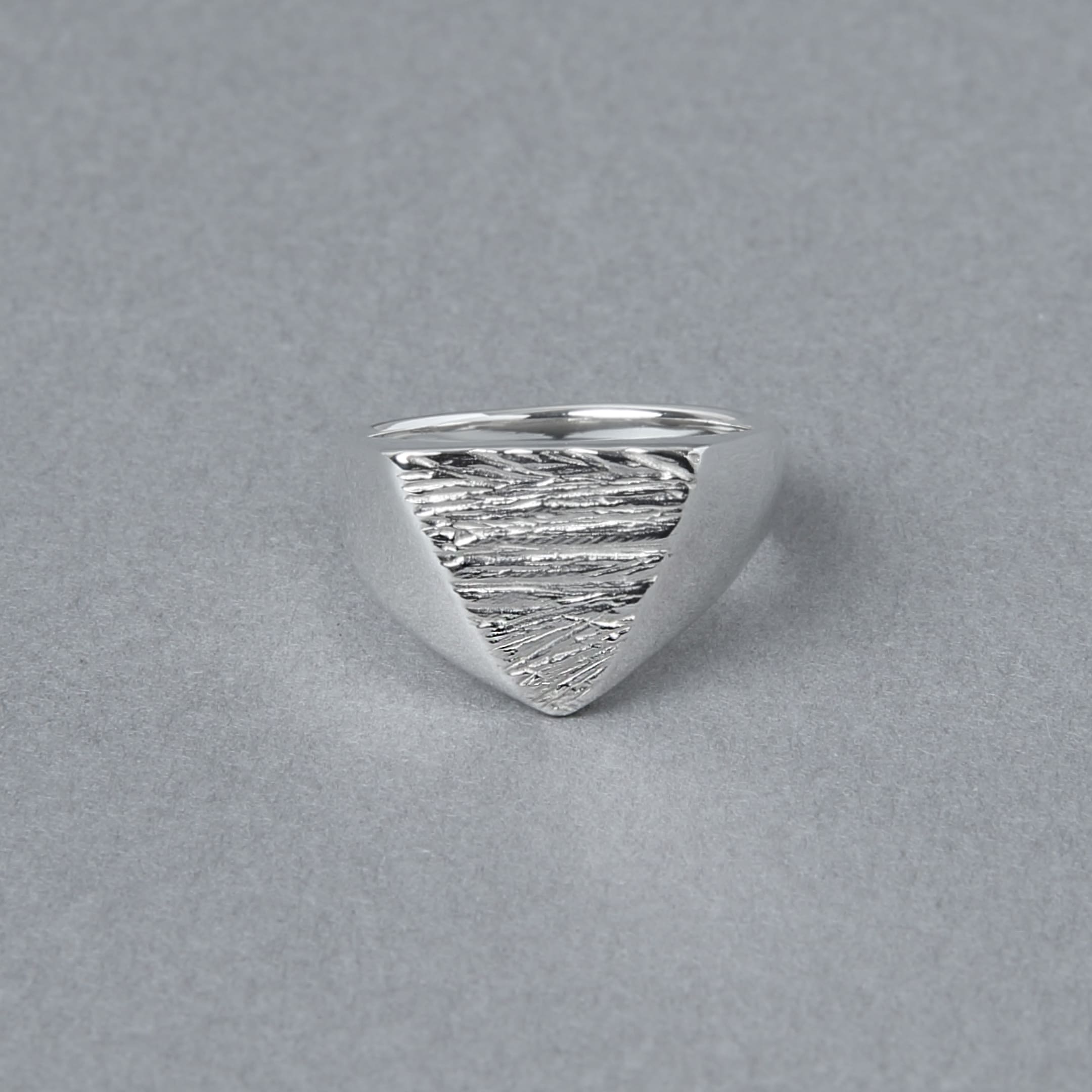 三角形のトップに木目のようなテクスチャが施されたシルバー925シグネットリング。正面から見た写真で、エッジの効いたフォルムが印象的。