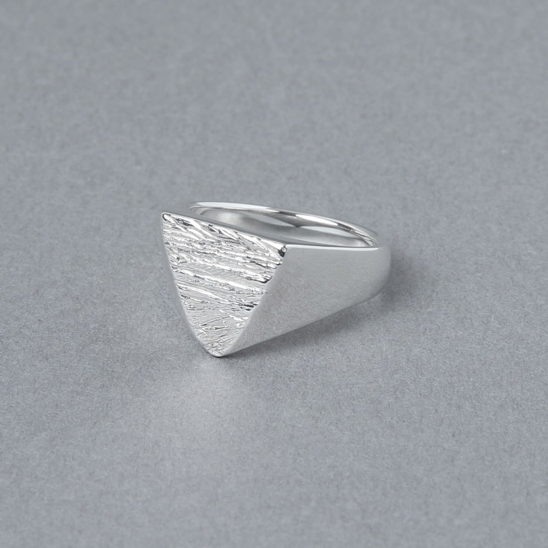 木目模様の三角形トップが特徴的なシルバーリングを斜め前から撮影。滑らかなラインと質感のコントラストが際立つ。