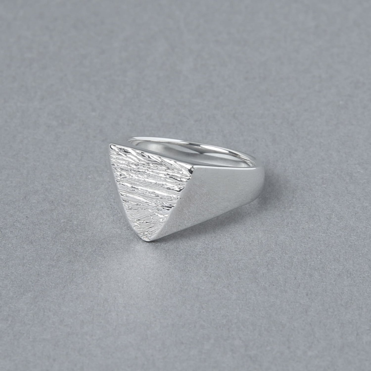 木目模様の三角形トップが特徴的なシルバーリングを斜め前から撮影。滑らかなラインと質感のコントラストが際立つ。