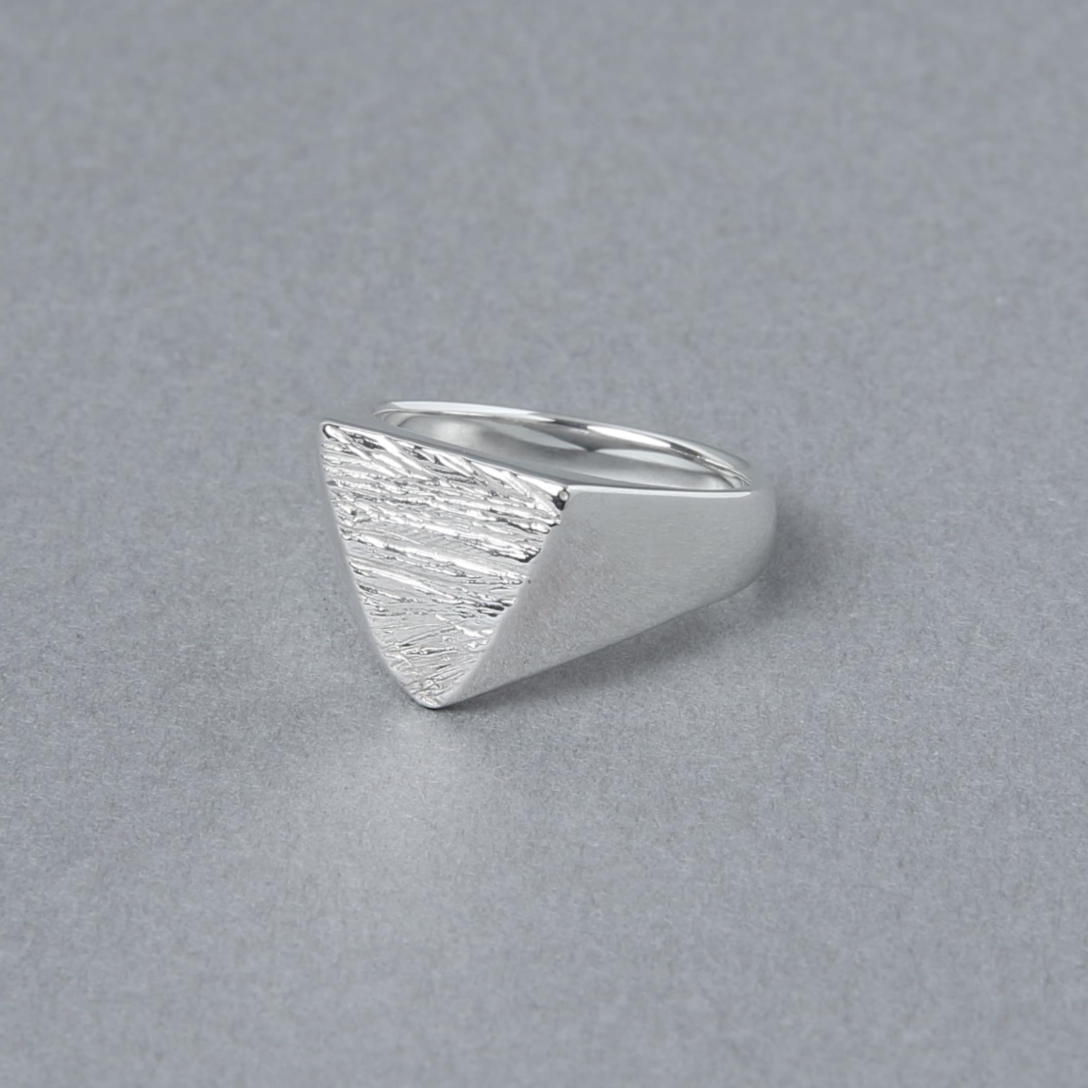 木目模様の三角形トップが特徴的なシルバーリングを斜め前から撮影。滑らかなラインと質感のコントラストが際立つ。