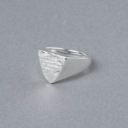 木目模様の三角形トップが特徴的なシルバーリングを斜め前から撮影。滑らかなラインと質感のコントラストが際立つ。