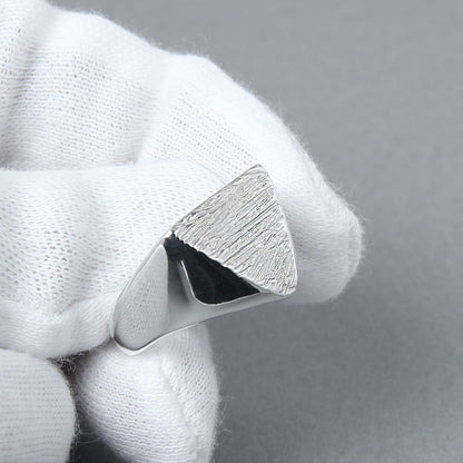 白い手袋を着けた手が、木目模様の三角形シグネットリングを持つ様子。職人による繊細なテクスチャと輝きが際立つディテールショット。