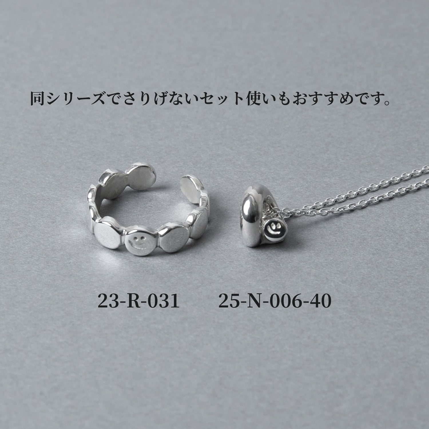 シルバー925製のスマイルモチーフ・ジュエリー。丸いプレートが連なるデザインリング（品番：23-R-031）と、ぷっくりとしたフォルムにスマイルが刻まれたネックレス（品番：25-N-006-40）が並んだ、セット使いの提案画像。