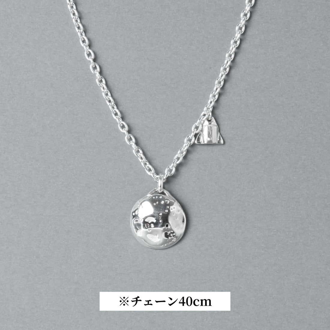 シルバー925製のネックレス。表面にクレーターのような凹凸を施した満月モチーフのトップと、小さなロケットのチャームが並ぶデザイン。