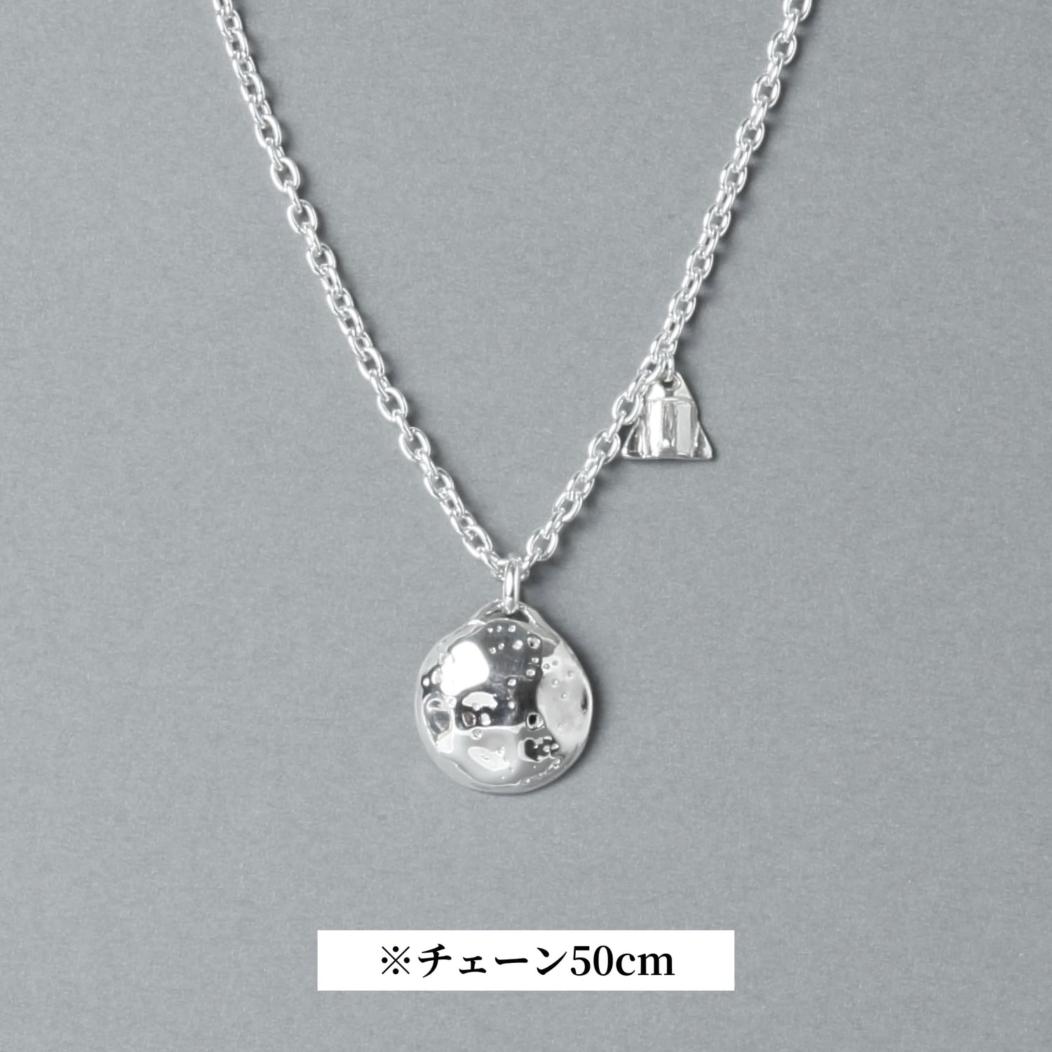 シルバー925製のネックレス。表面にクレーターのような凹凸を施した満月モチーフのトップと、小さなロケットのチャームが並ぶデザイン。