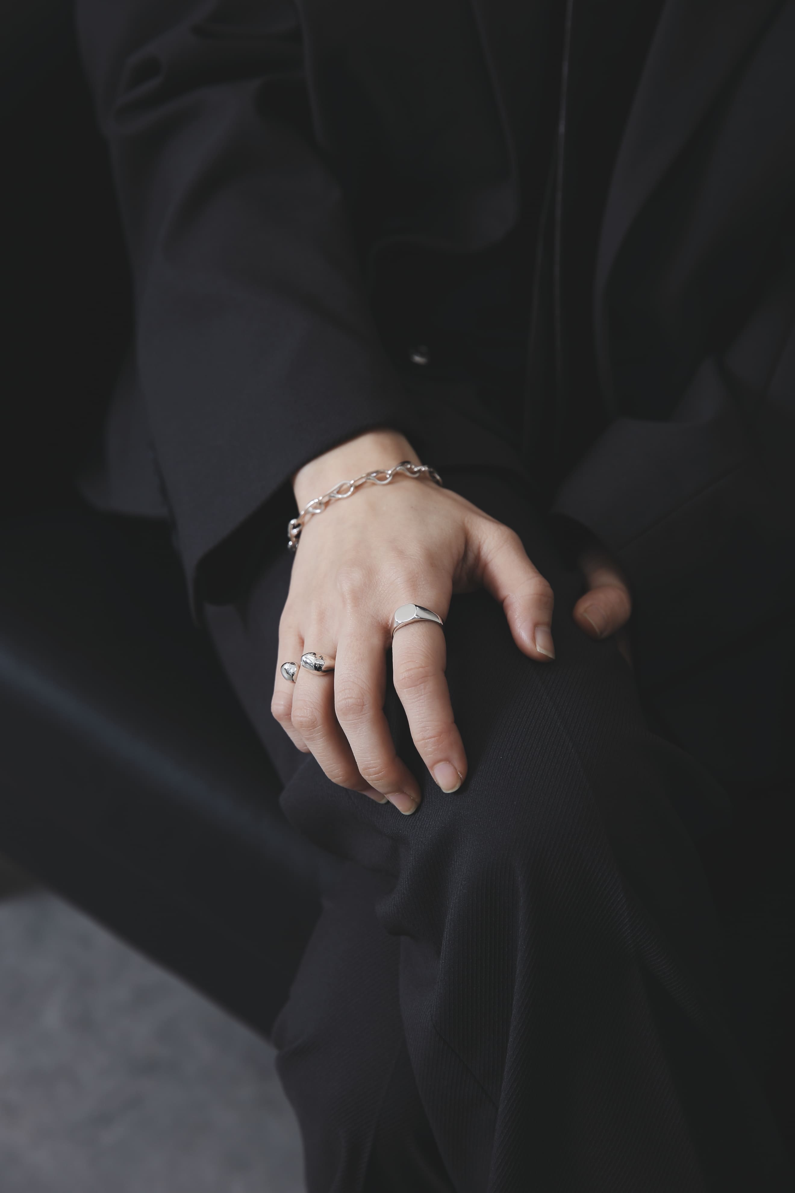 膝の上に手を置いたスタイルカット。シルバー925のリングとチェーンブレスレットが上品な存在感を放ち、静かな強さを感じさせる。