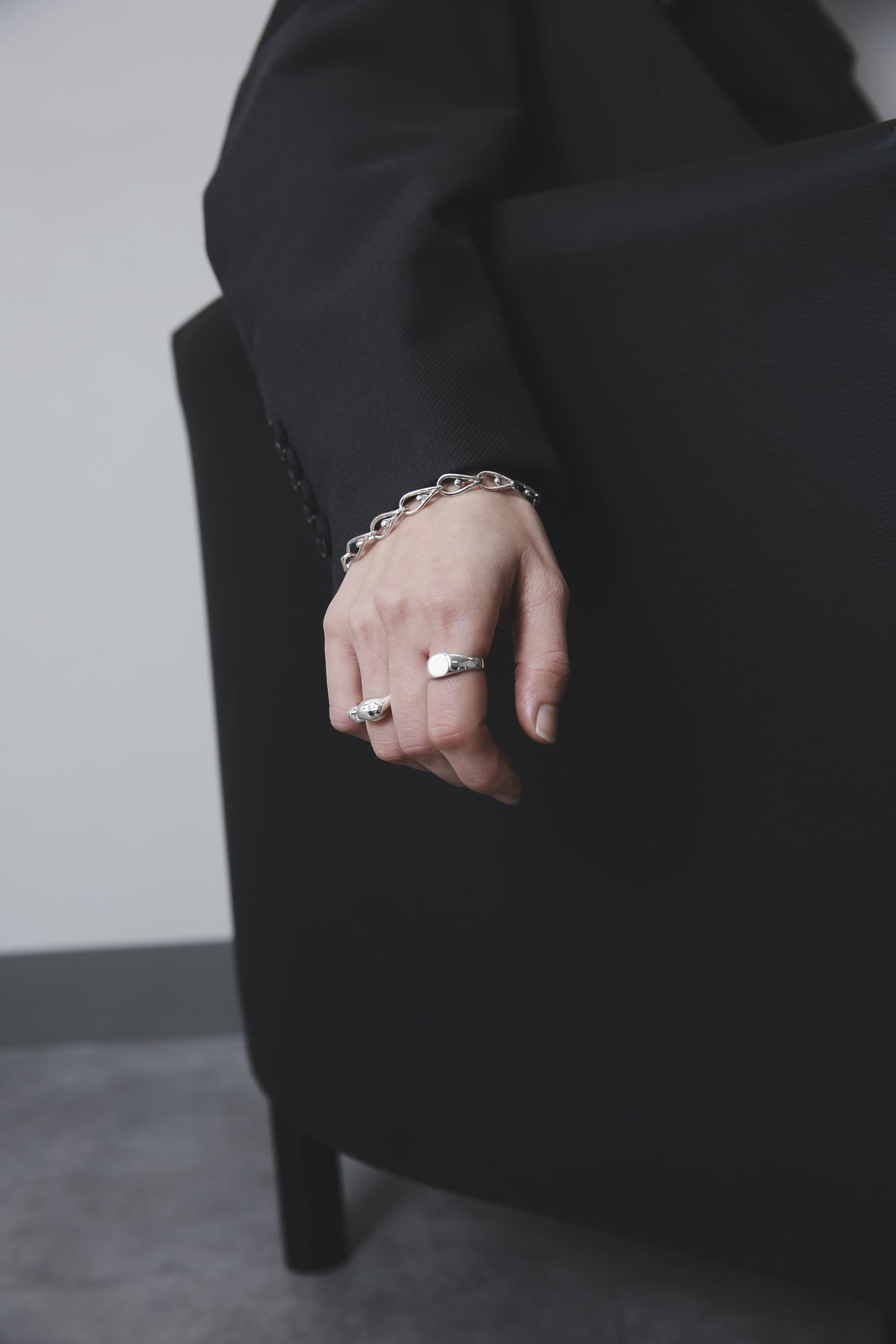 ソファの背に手をかけた構図。ラウンドシグネットリングとボリュームのあるオープンリングが、モードな黒の装いに映える。