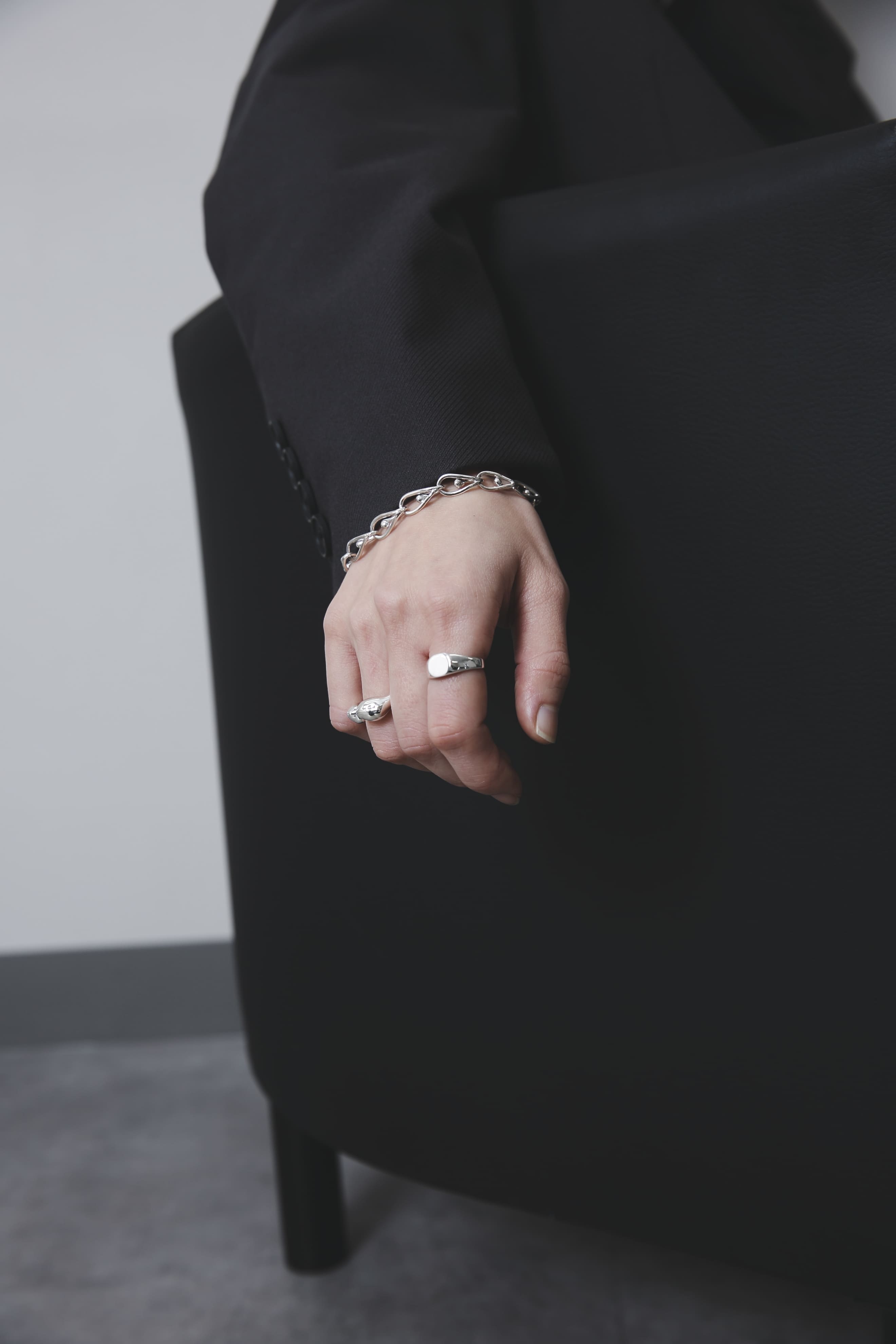 ソファの背に手をかけた構図。ラウンドシグネットリングとボリュームのあるオープンリングが、モードな黒の装いに映える。