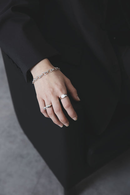 斜め上から捉えた手元。滑らかな曲線のシグネットリングと有機的フォルムのリングが、質感のコントラストを際立たせている。